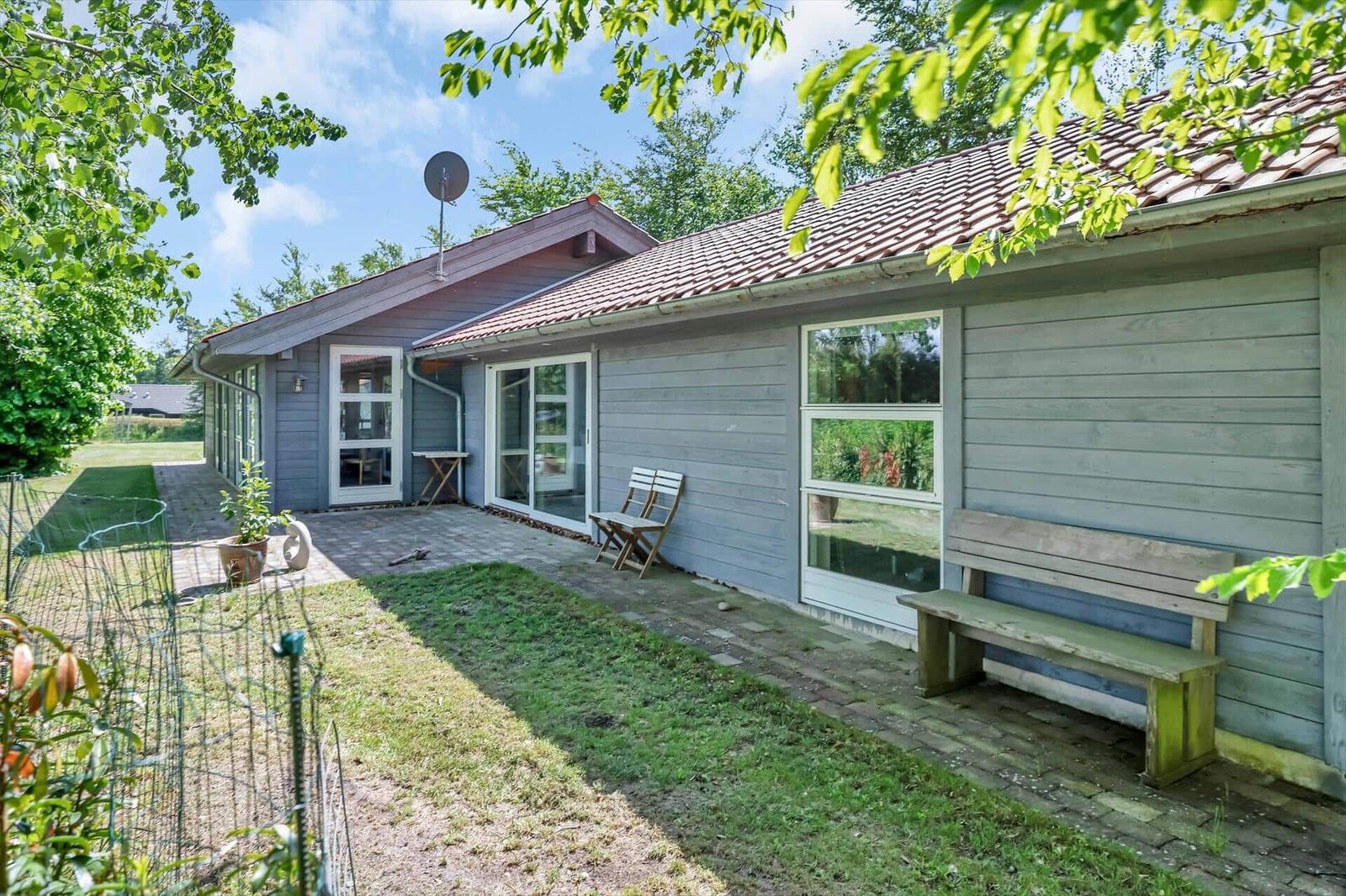 Ein Haus mit Holzfassade, Terrasse und Garten. Ein Holzstuhl und eine Bank stehen draußen.