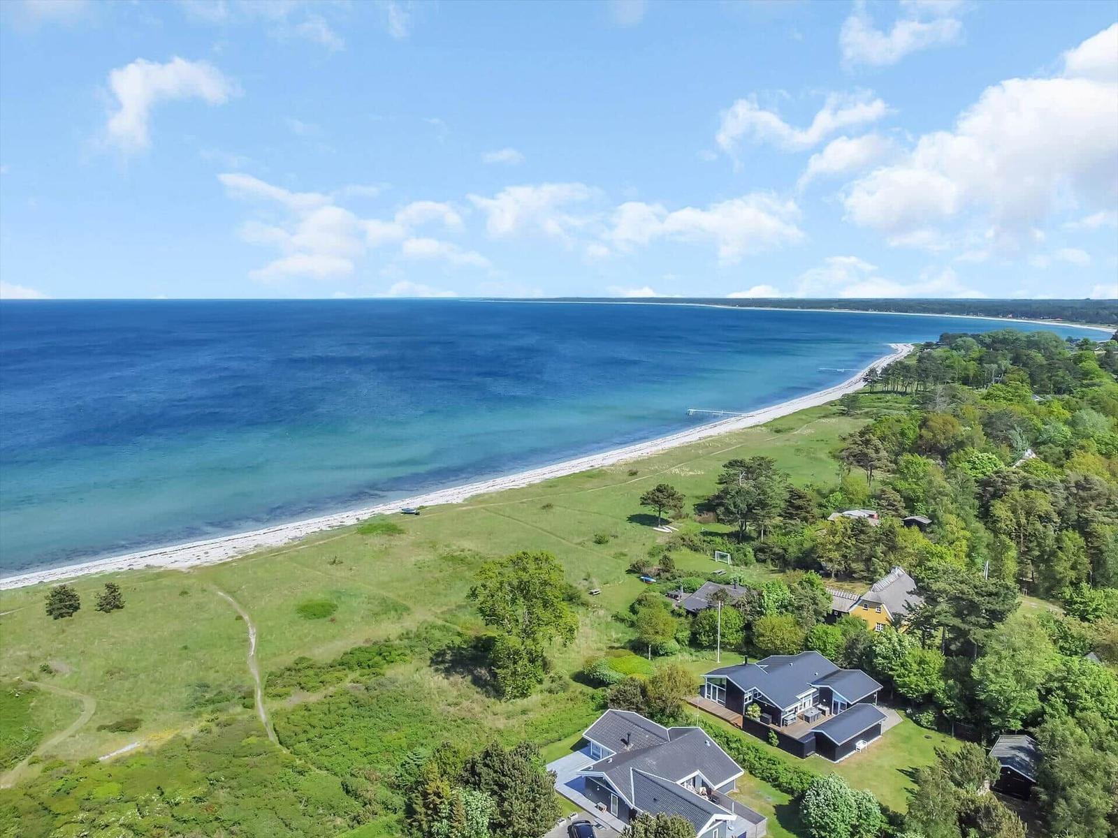Meerstrand mit grünen Wiesen und Häusern in der Ferne.