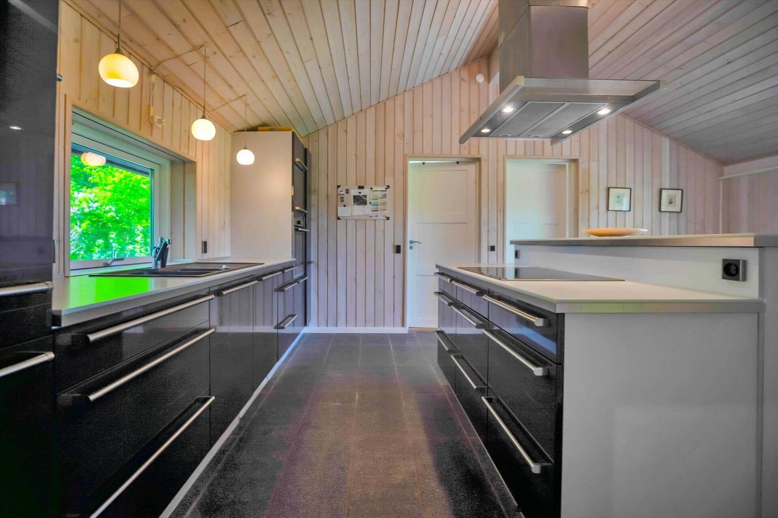 Moderne Küche mit Holzwänden, schwarzen Schränken und Fensterblick auf Grün.