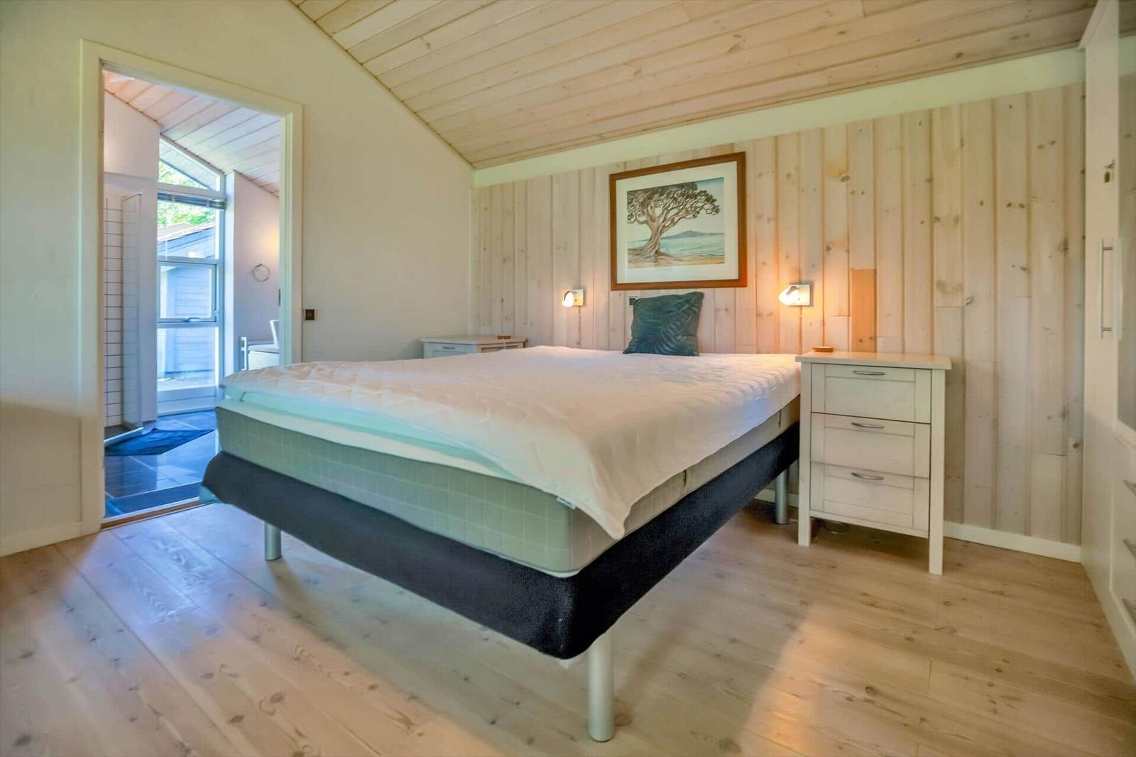 Schlafzimmer mit Bett, Nachttisch und Holzwand. Tür führt in Badezimmer.