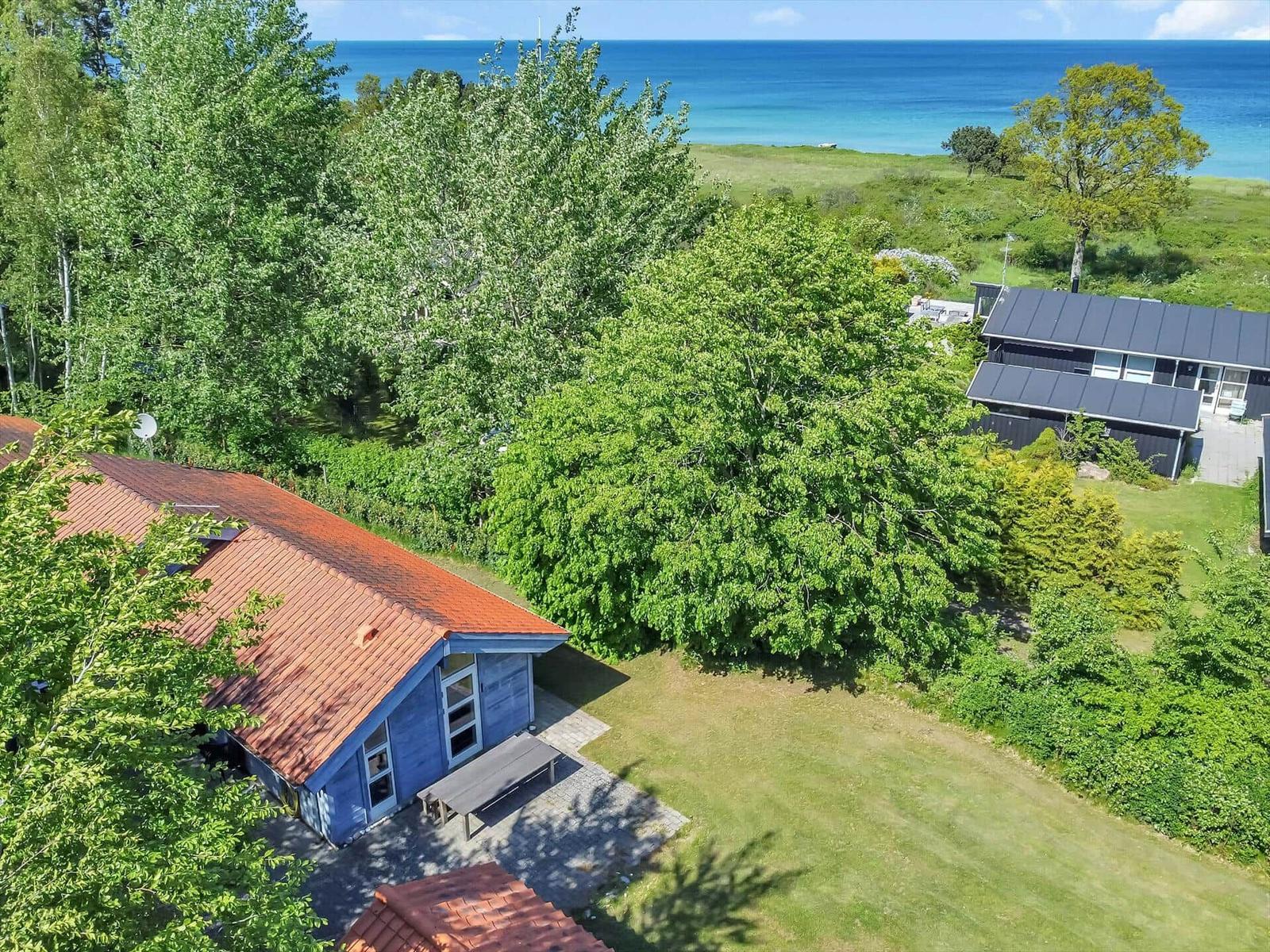 Haus mit rotem Dach, umgeben von Bäumen und Gras, mit Blick auf das Meer.