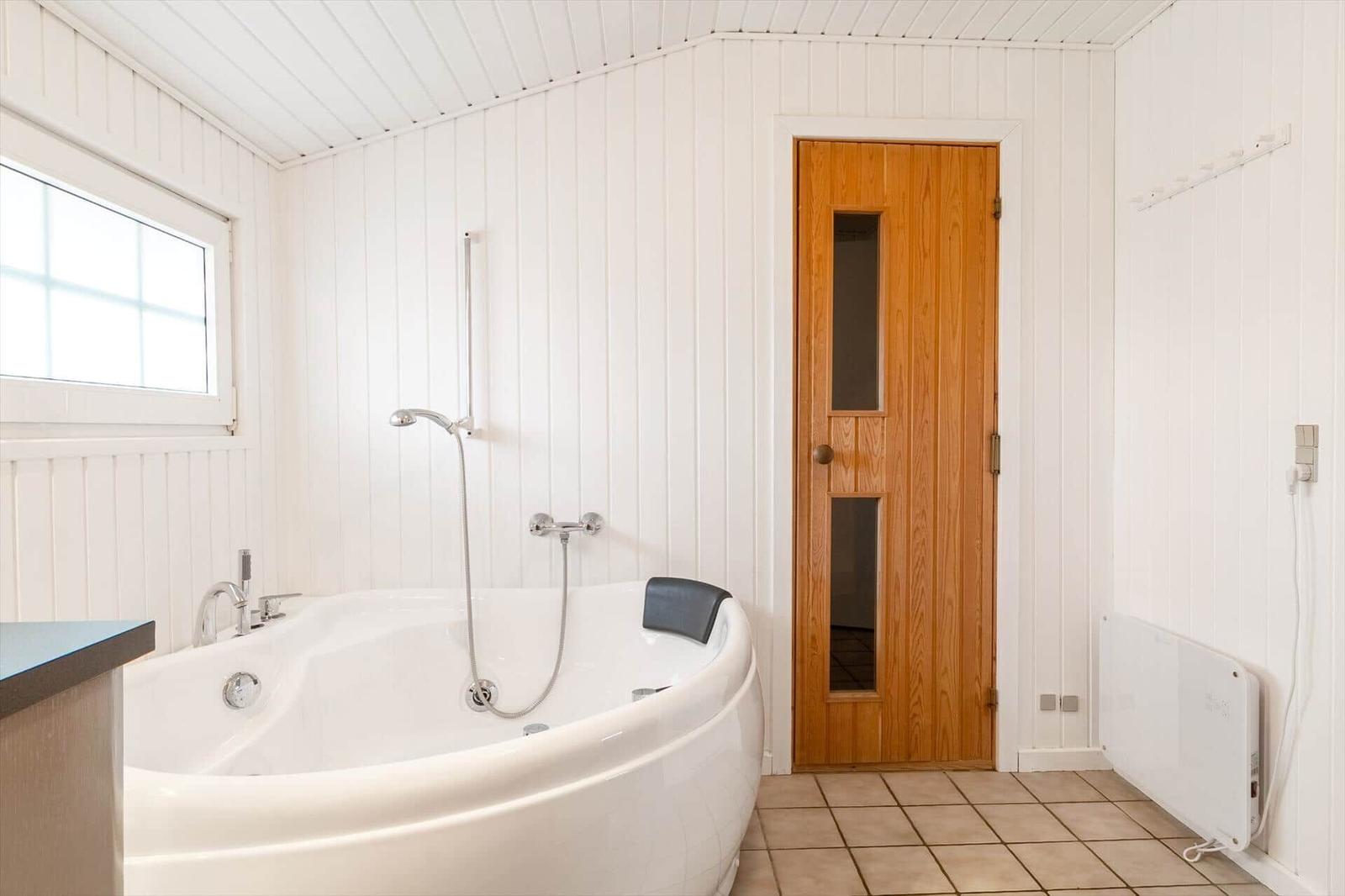 Bad mit Whirlpool, Holztür und Fenster. Weiße Wände, Fliesenboden und Heizkörper.