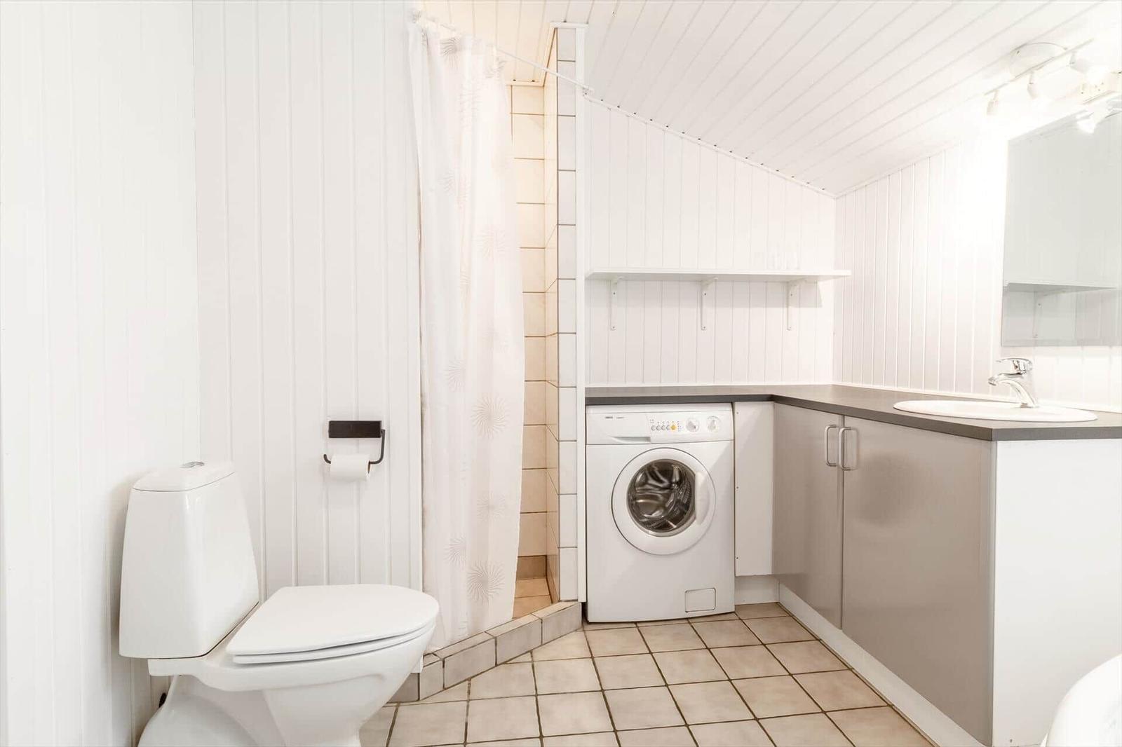 Bad mit Toilette, Dusche, Waschmaschine und Waschbecken.
