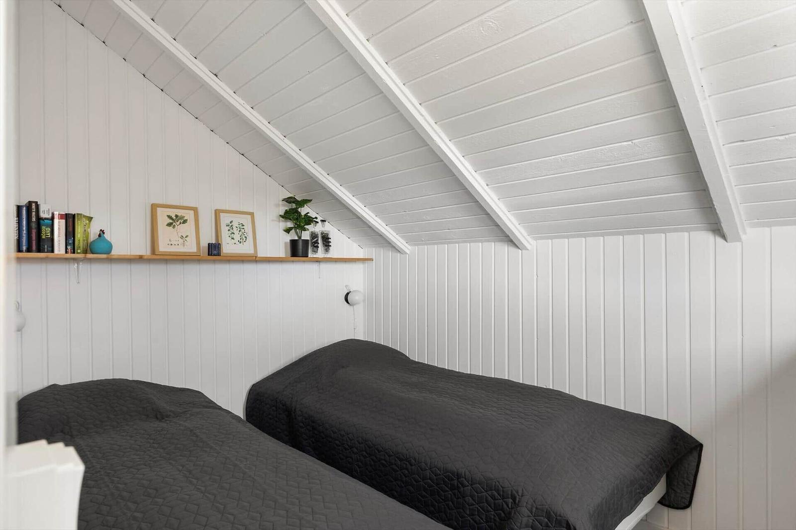 Zwei Betten unter einer schrägen Decke mit weißen Wänden und einer Holzregalwand.