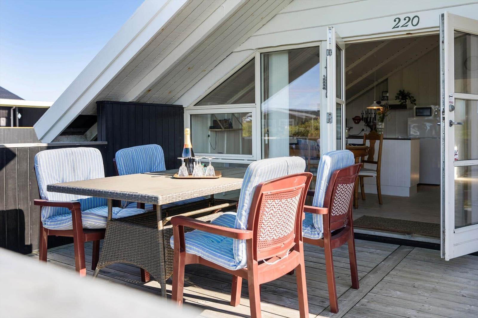 Terrasse mit Tisch und Stühlen, Tür führt ins Innere der Unterkunft.