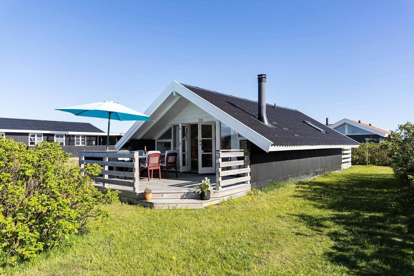 Ein Haus mit Terrasse, blauem Sonnenschirm und Garten.
