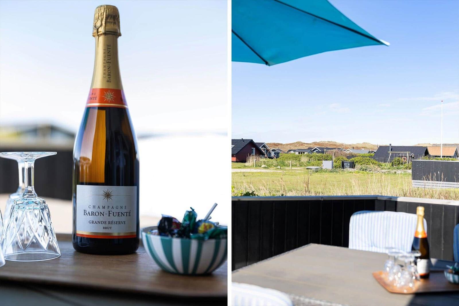 Eine Flasche Champagner und Gläser auf einer Terrasse mit Blick auf Häuser und Dünen.