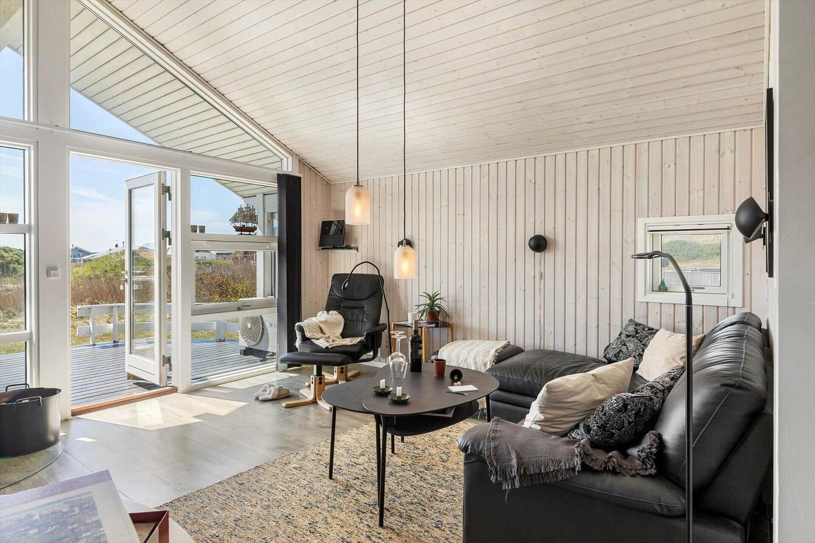 Wohnraum mit Ledersofa, Tisch und Sessel. Durchgang zur Terrasse mit Blick auf die Landschaft.