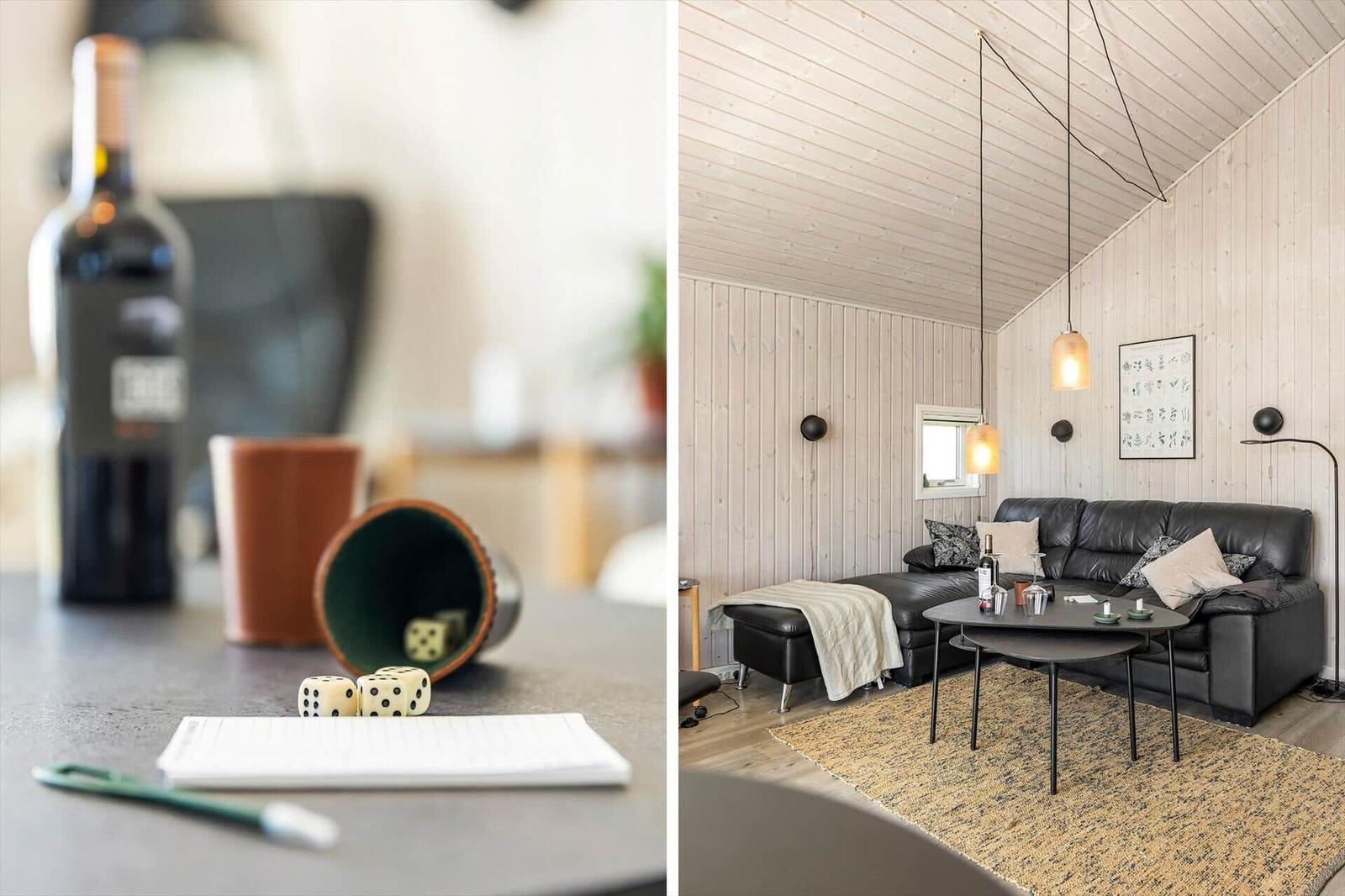 Ein Wohnzimmer mit schwarzem Sofa, Holzwand und Hängelampe. Auf Tisch stehen Gläser und eine Flasche.