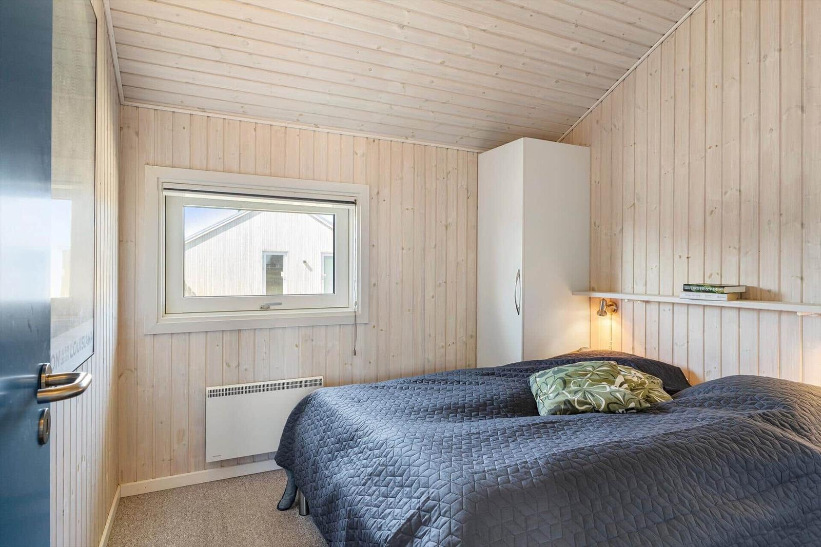 Schlafzimmer mit Holzwänden, Bett, Kleiderschrank und Fenster.