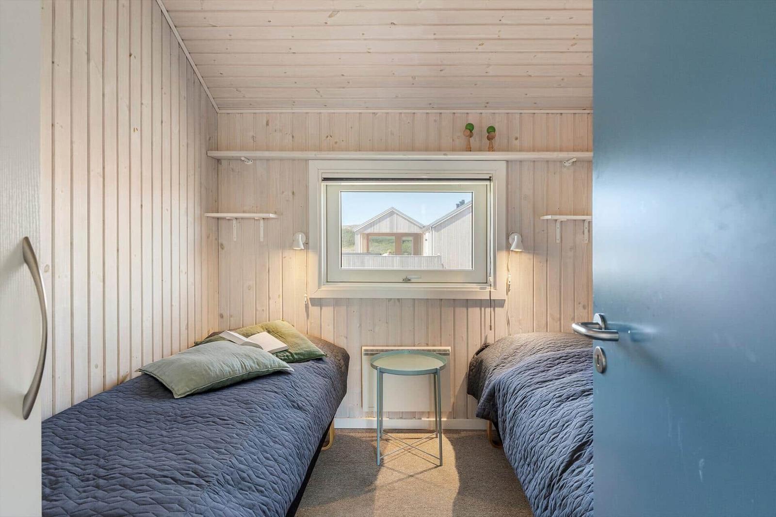 Zwei Betten in einem Zimmer mit Holzwand und Fenster. Kleiner Tisch zwischen den Betten.