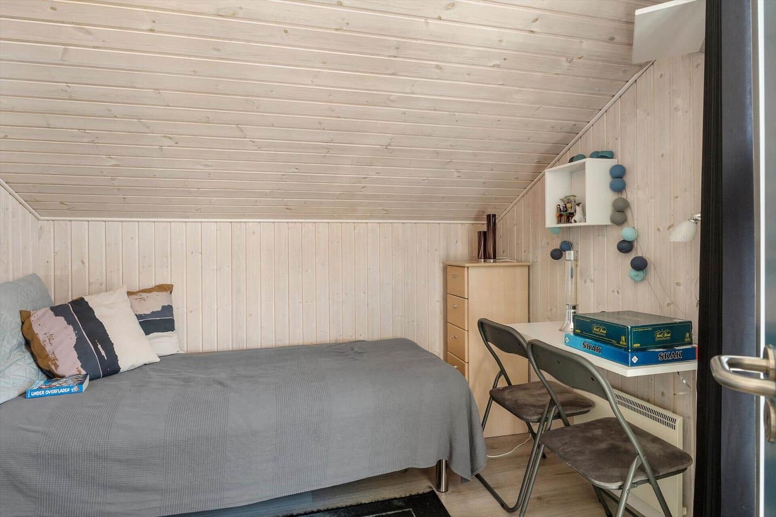 Schlafzimmer mit Bett, Schreibtisch und Kleiderschrank. Holzwände und -decke.