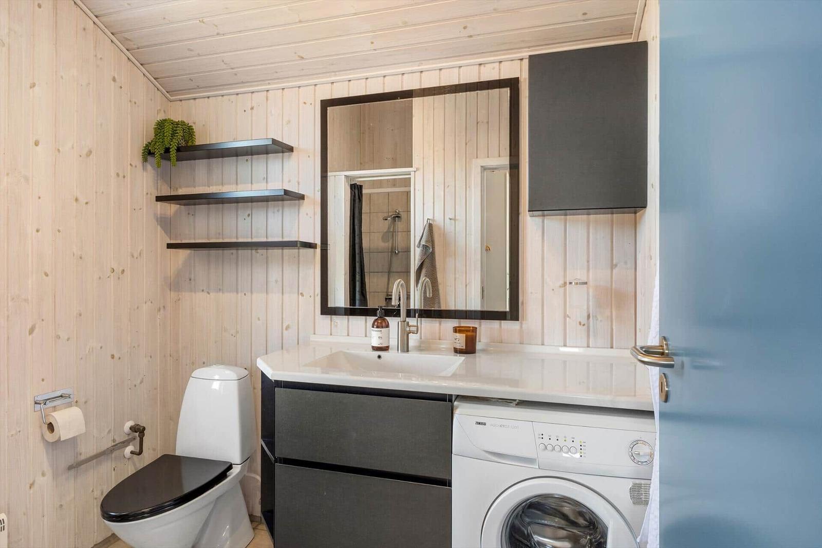Badezimmer mit Waschmaschine, Spiegel und Toilette an Holzwand