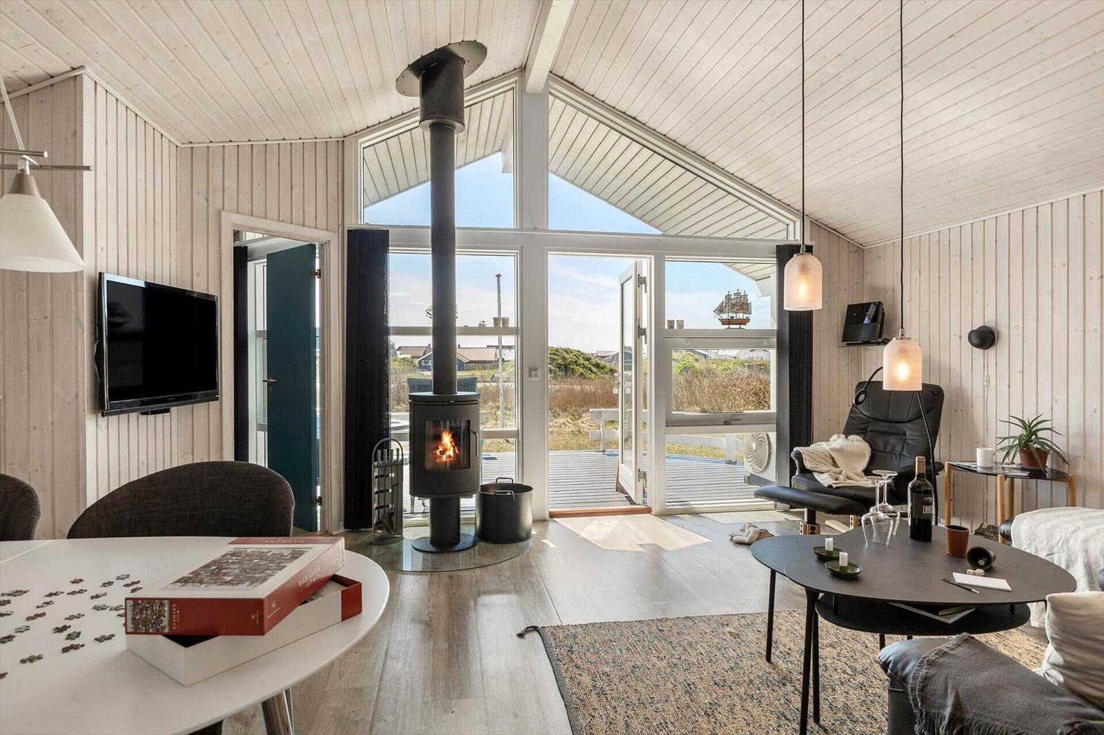 Wohnraum mit Kamin, TV und Blick auf Terrasse.