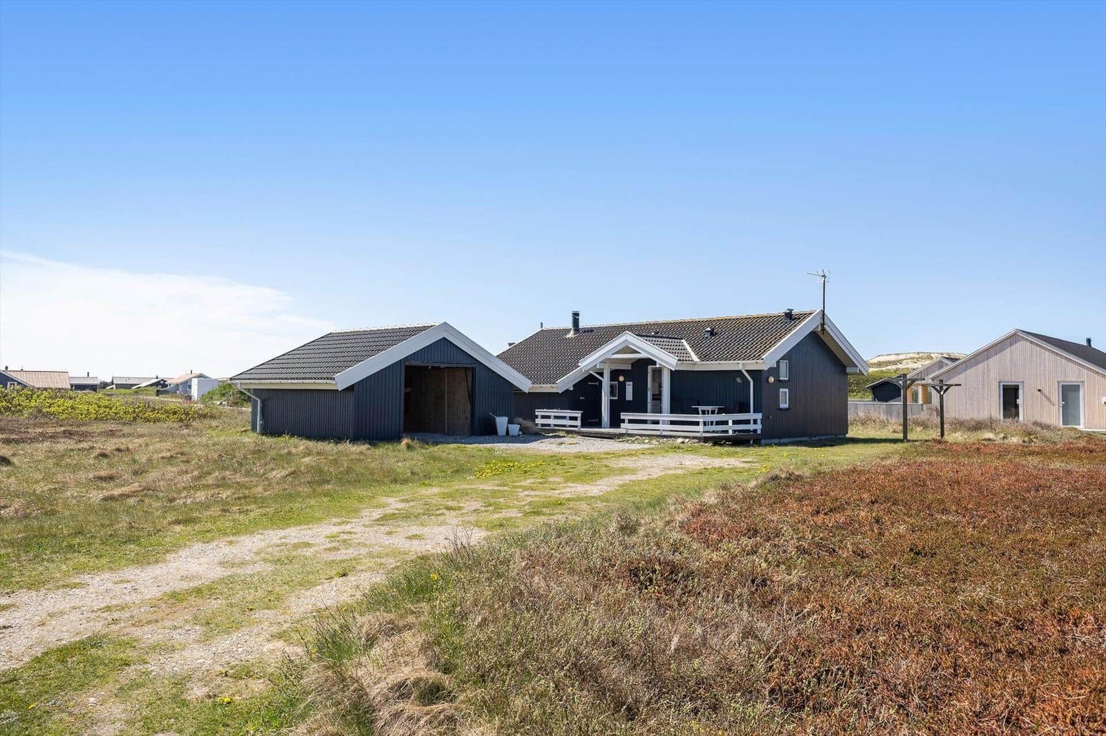 Ein dunkelgrauer Holzhaus mit weißer Veranda und Terrasse in einer grasbewachsenen Landschaft.