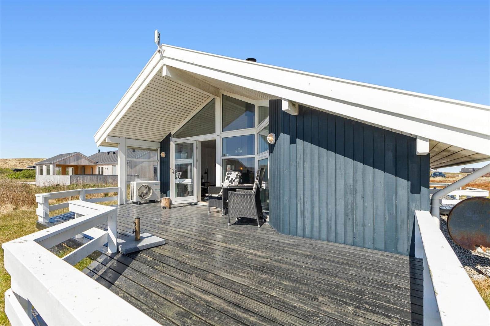 Haus mit Terrasse, Glasfront und dunkler Holzfassade unter blauem Himmel.