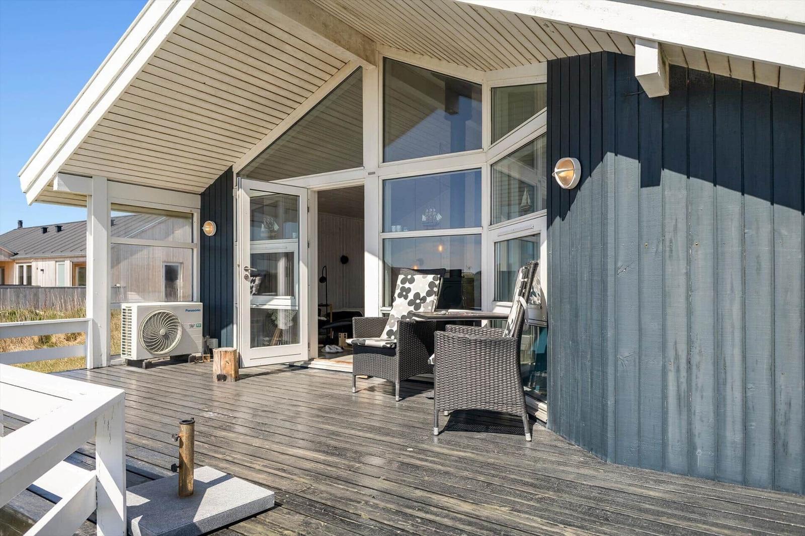Terrasse mit Sitzgelegenheit und Blick ins Haus. Holzdeck und blaue Fassade.