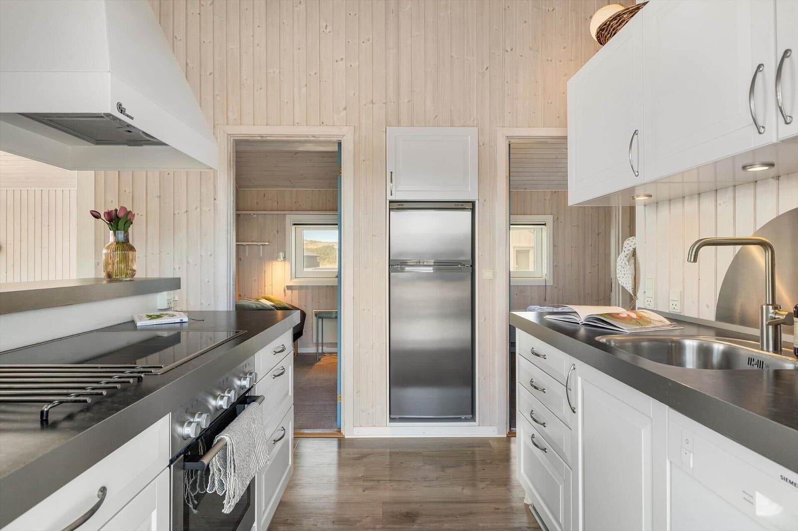 Küche mit Edelstahl-Kühlschrank, weißen Schränken und Holzwandverkleidung.