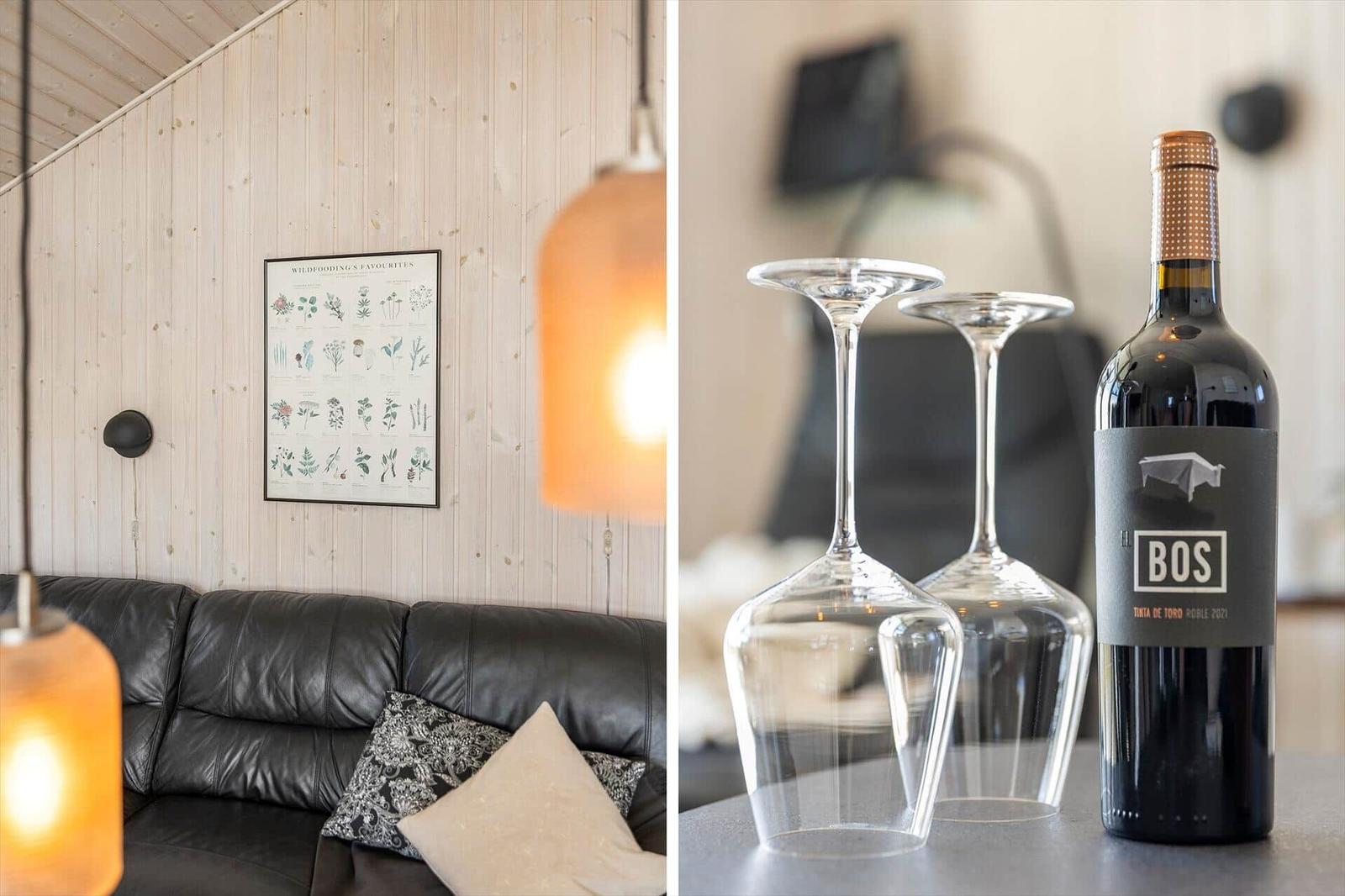 Schwarzes Sofa mit Kissen an Holzwand. Weinglas und Flasche auf Tisch.