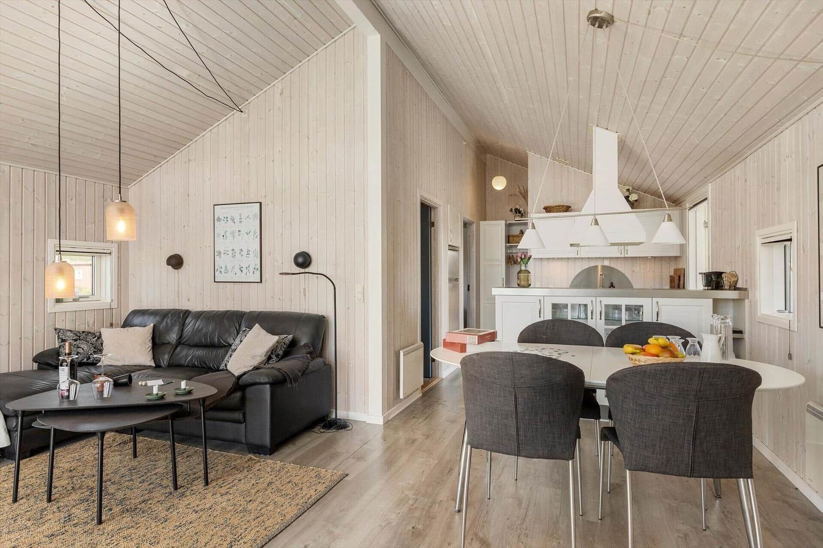 Wohn- und Essbereich mit Sofa, Tisch und Küchenzeile. Holzwände und -decke.