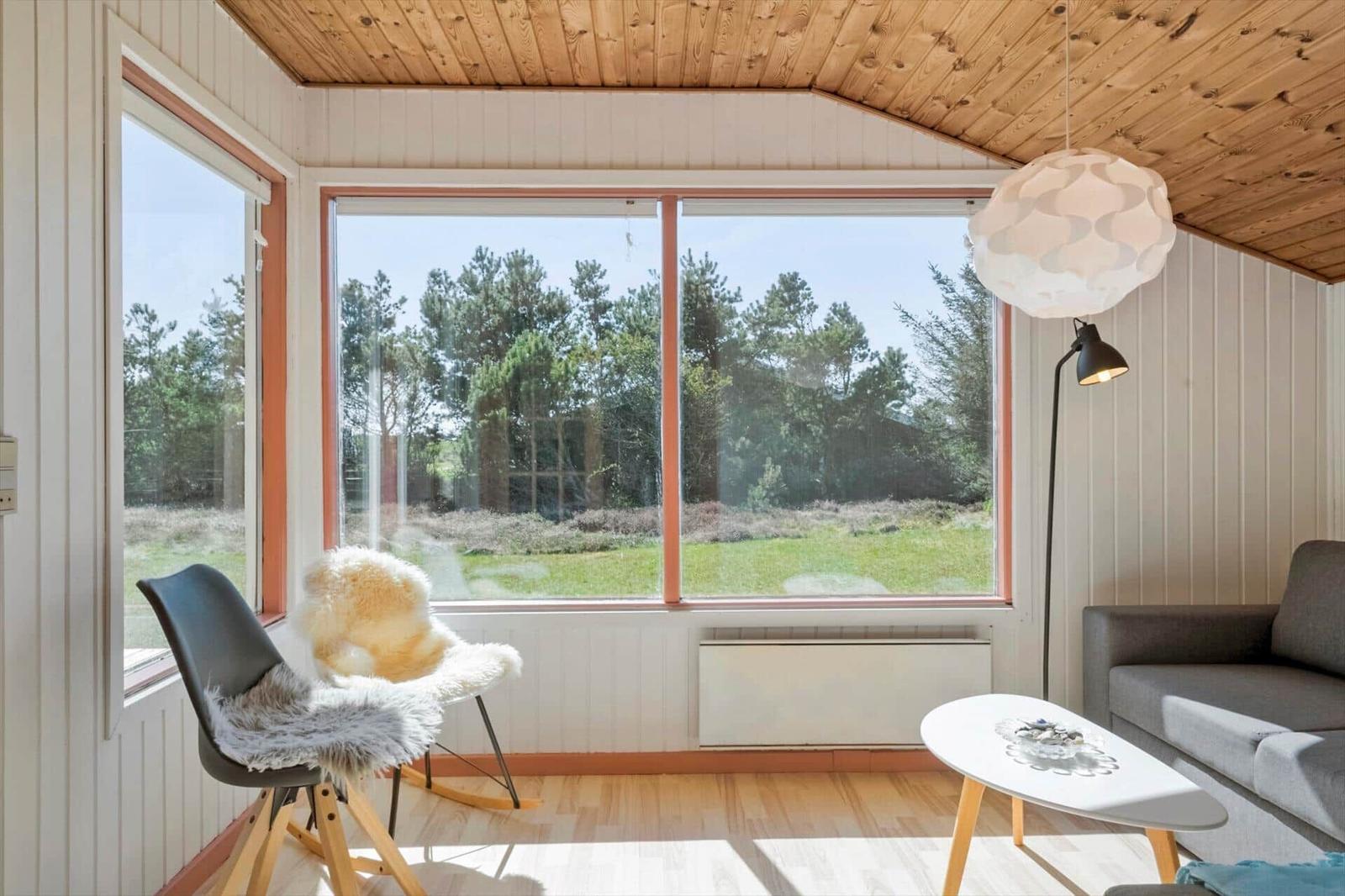 Wohnzimmer mit Holzdecke, großem Fenster und Sitzgelegenheiten.