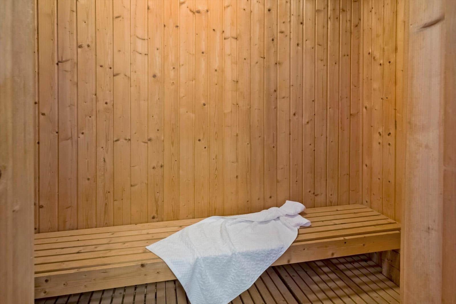 Sauna mit Holzwand und Bank, darauf liegt eine weiße Decke.