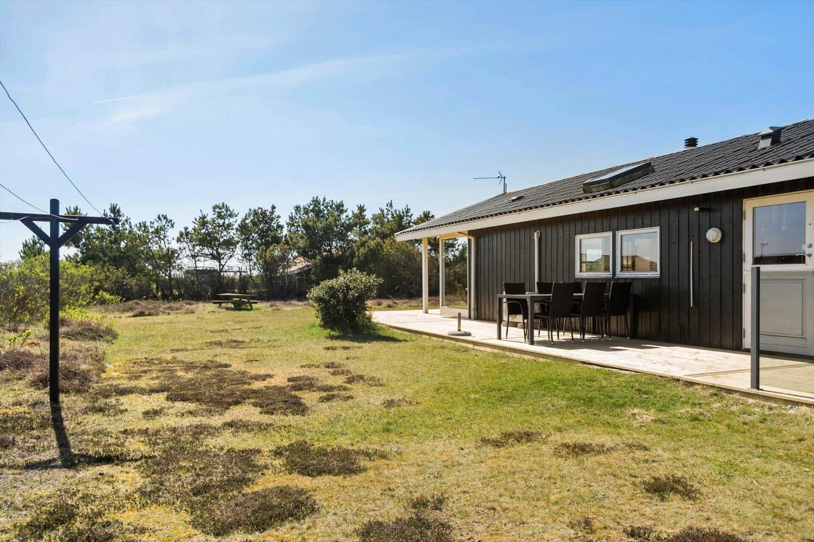 Ein Haus mit Terrasse und Garten. Tisch und Stühle stehen draußen.