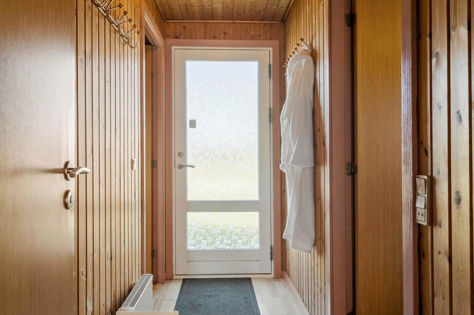 Eingangsbereich mit Holzwänden, Tür und Bademantel an der Wand.