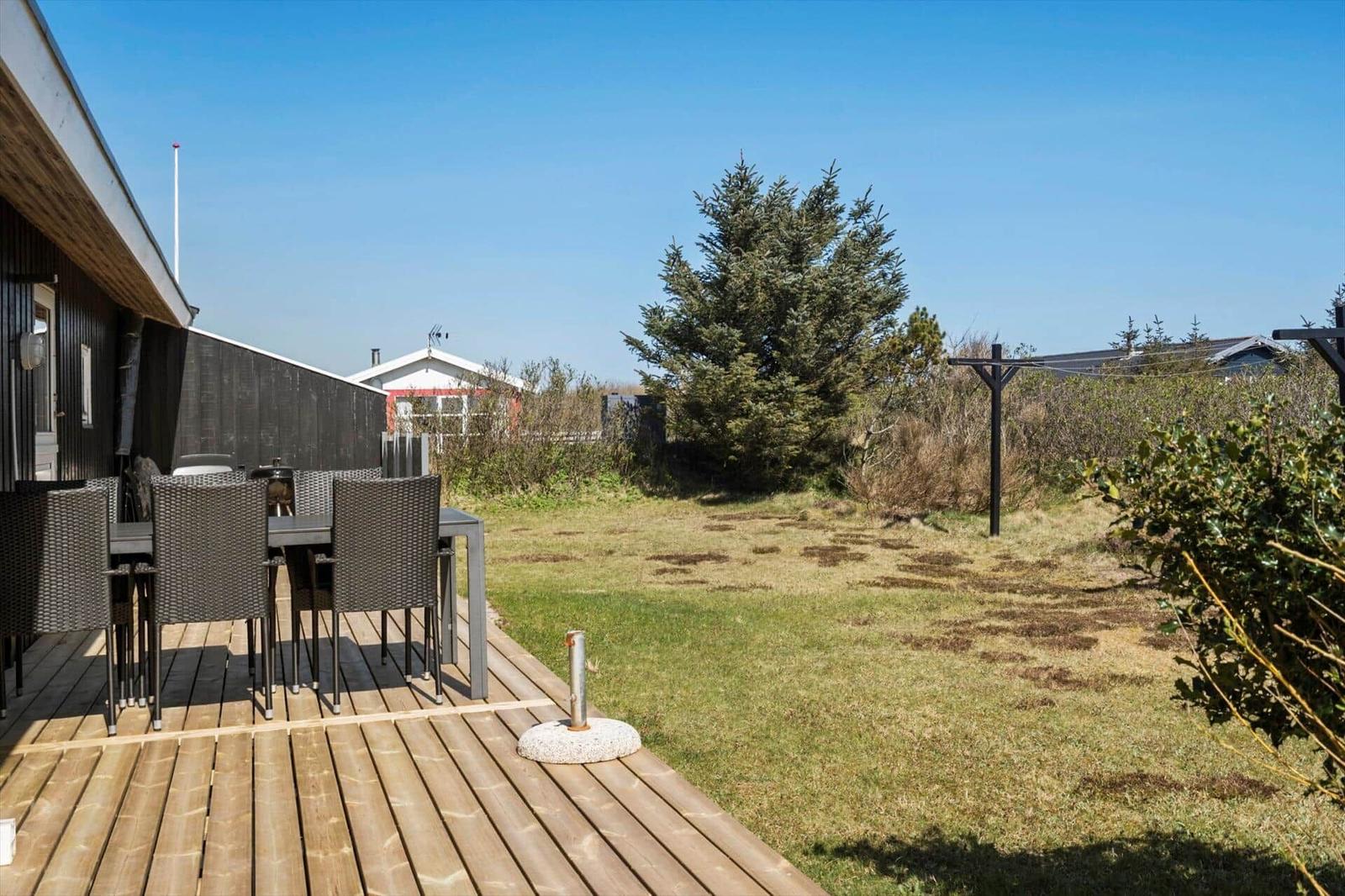 Terrasse mit Tisch und Stühlen, Grasfläche und Baum im Hintergrund.