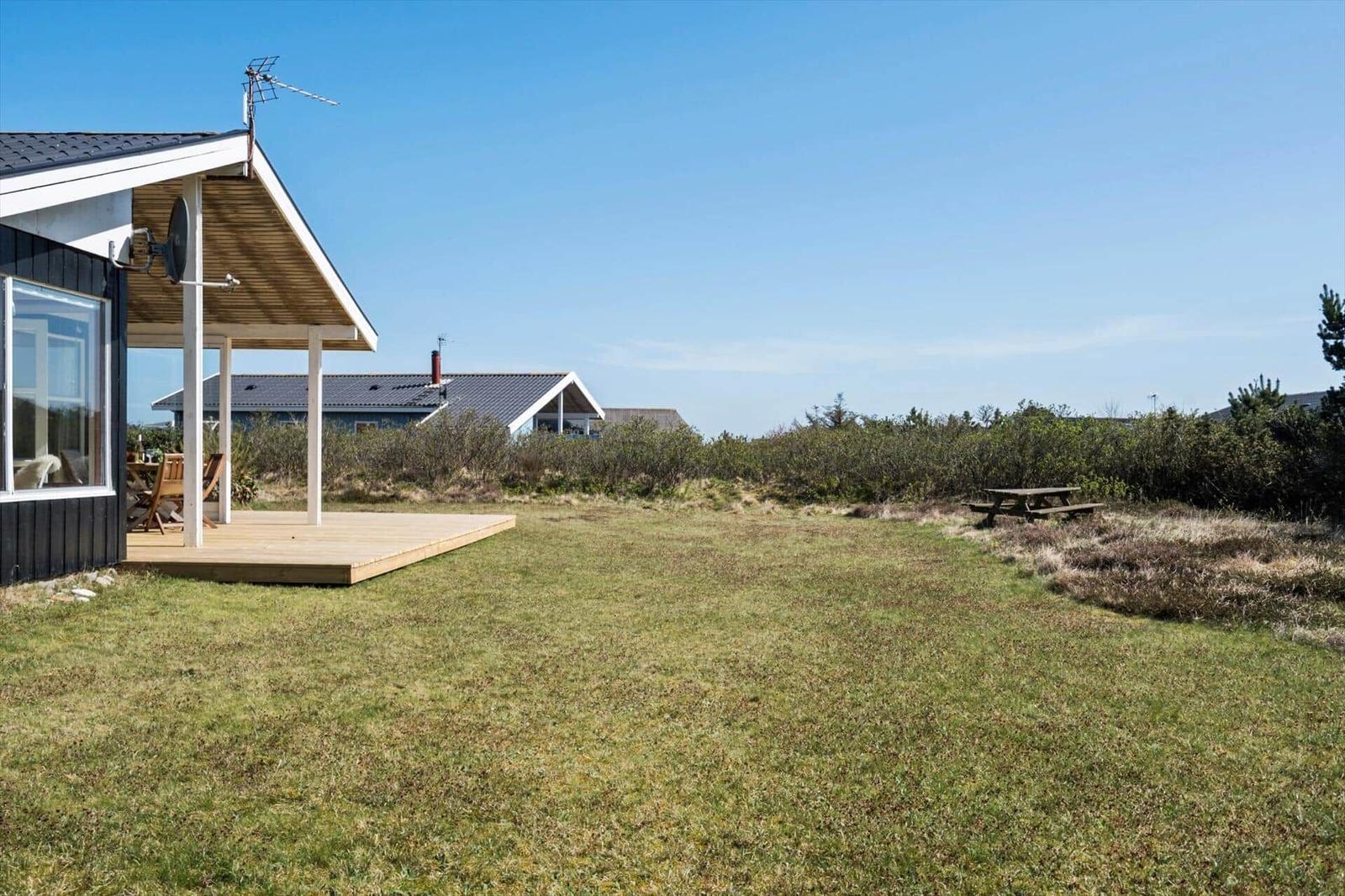 Haus mit Holzterrasse und großem Grünbereich. Im Hintergrund weitere Häuser.