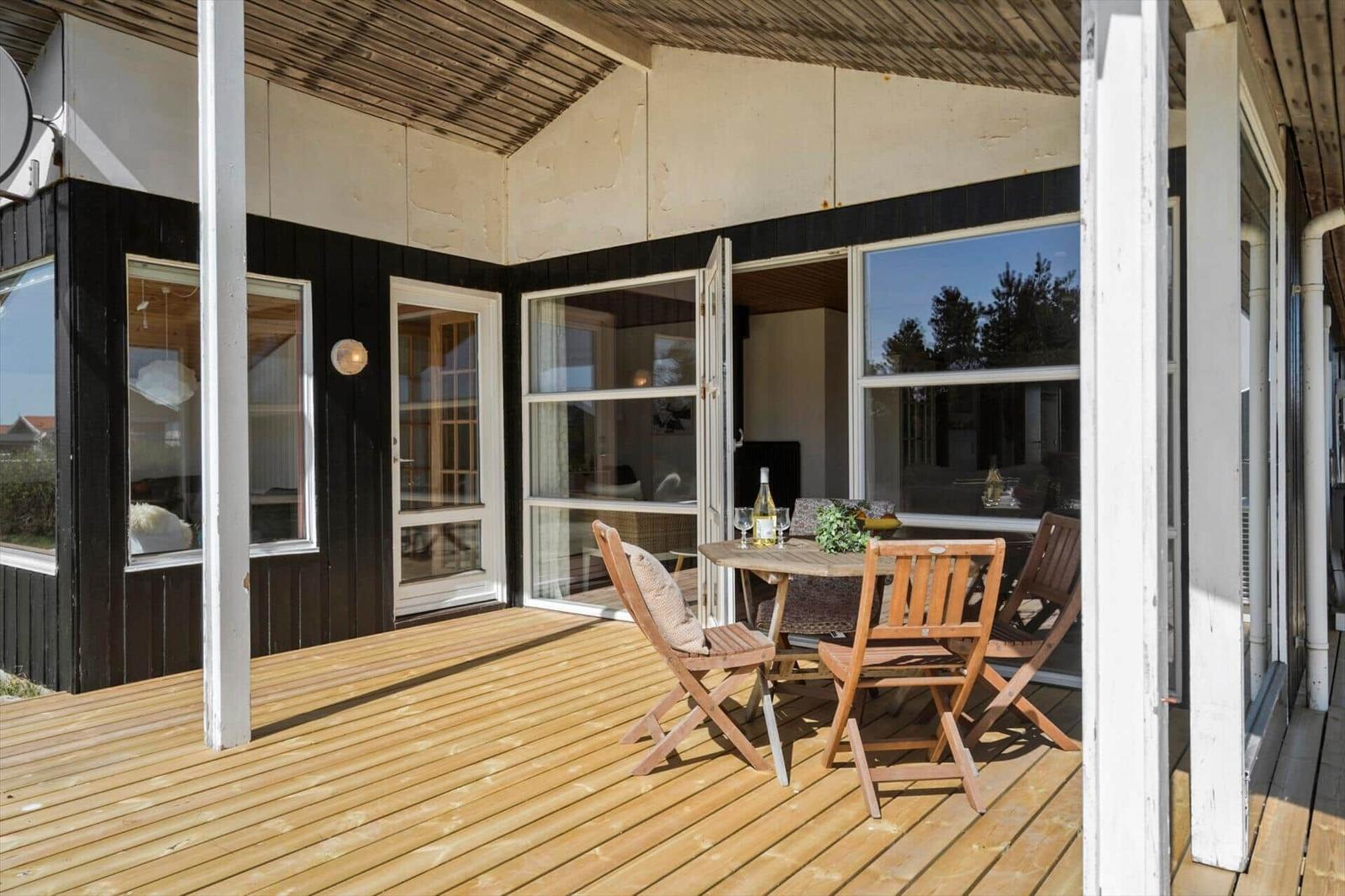 Terrasse mit Holzdielen, Tisch und Stühlen. Durchgehendes Fenster mit Blick ins Haus.