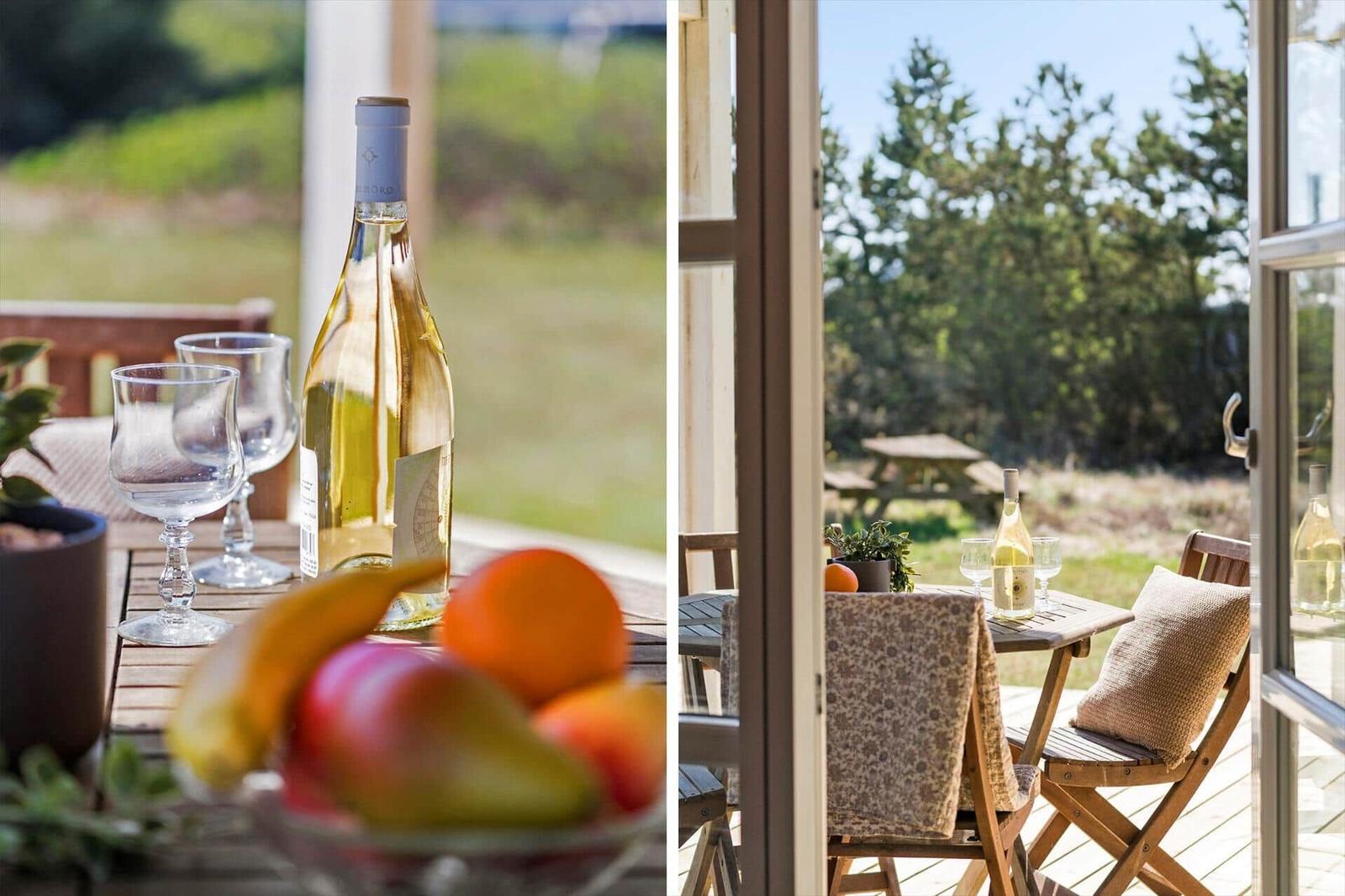 Terrasse mit Tisch, Stühlen und Weinflasche. Blick auf grüne Landschaft.
