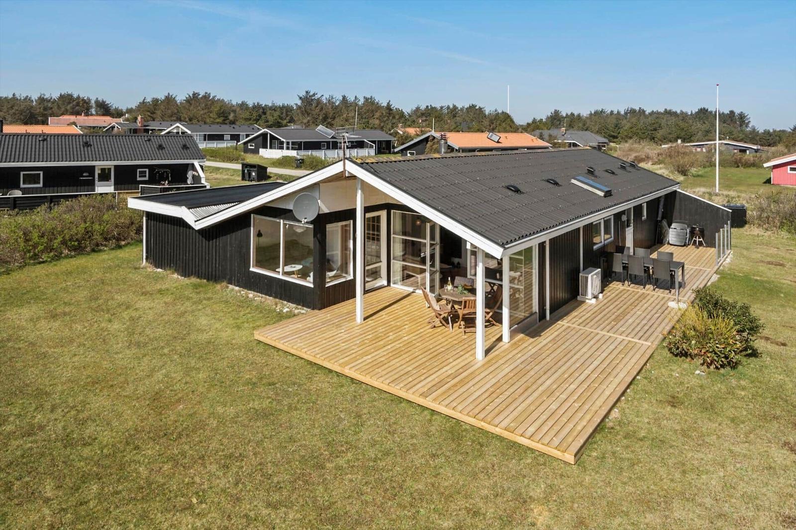 Moderne Villa mit Holzterrasse und großzügigem Außenbereich. Blick auf Grasland und Nachbarhäuser.