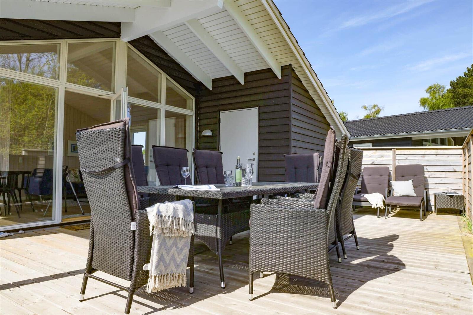 Terrasse mit Esstisch und Stühlen, Holzboden, großes Fenster, Himmel klar.