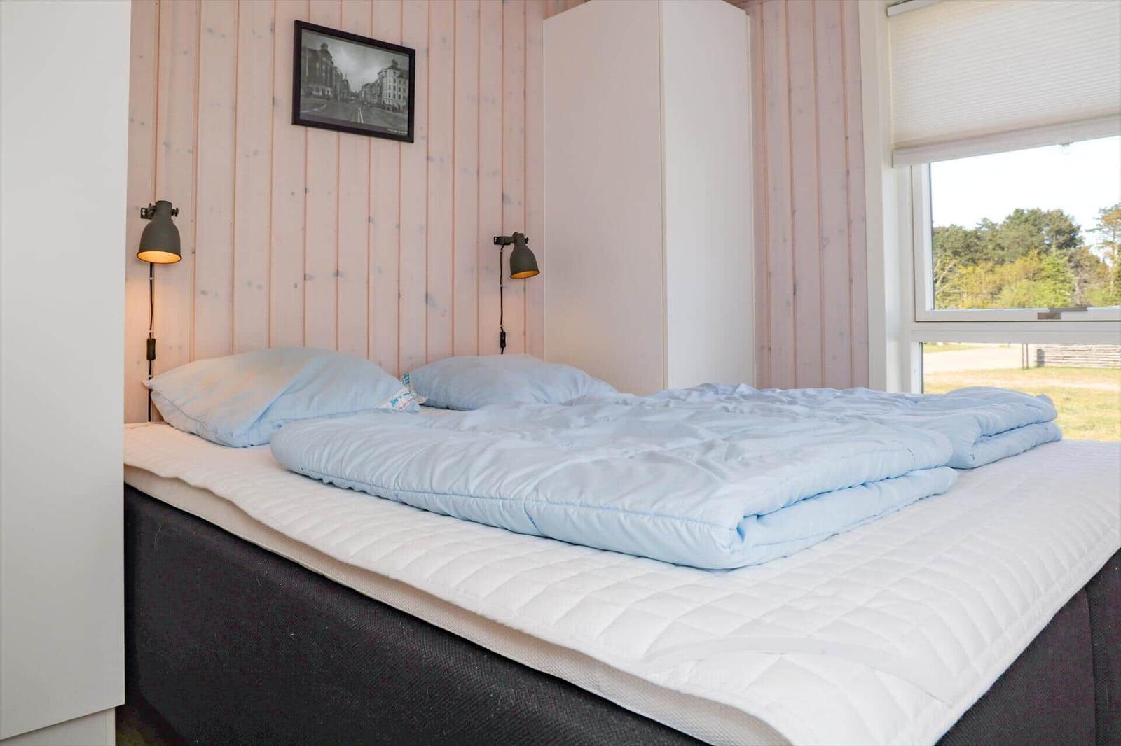 Schlafzimmer mit Bett, Wandlampen und Fensterblick auf Grünfläche.