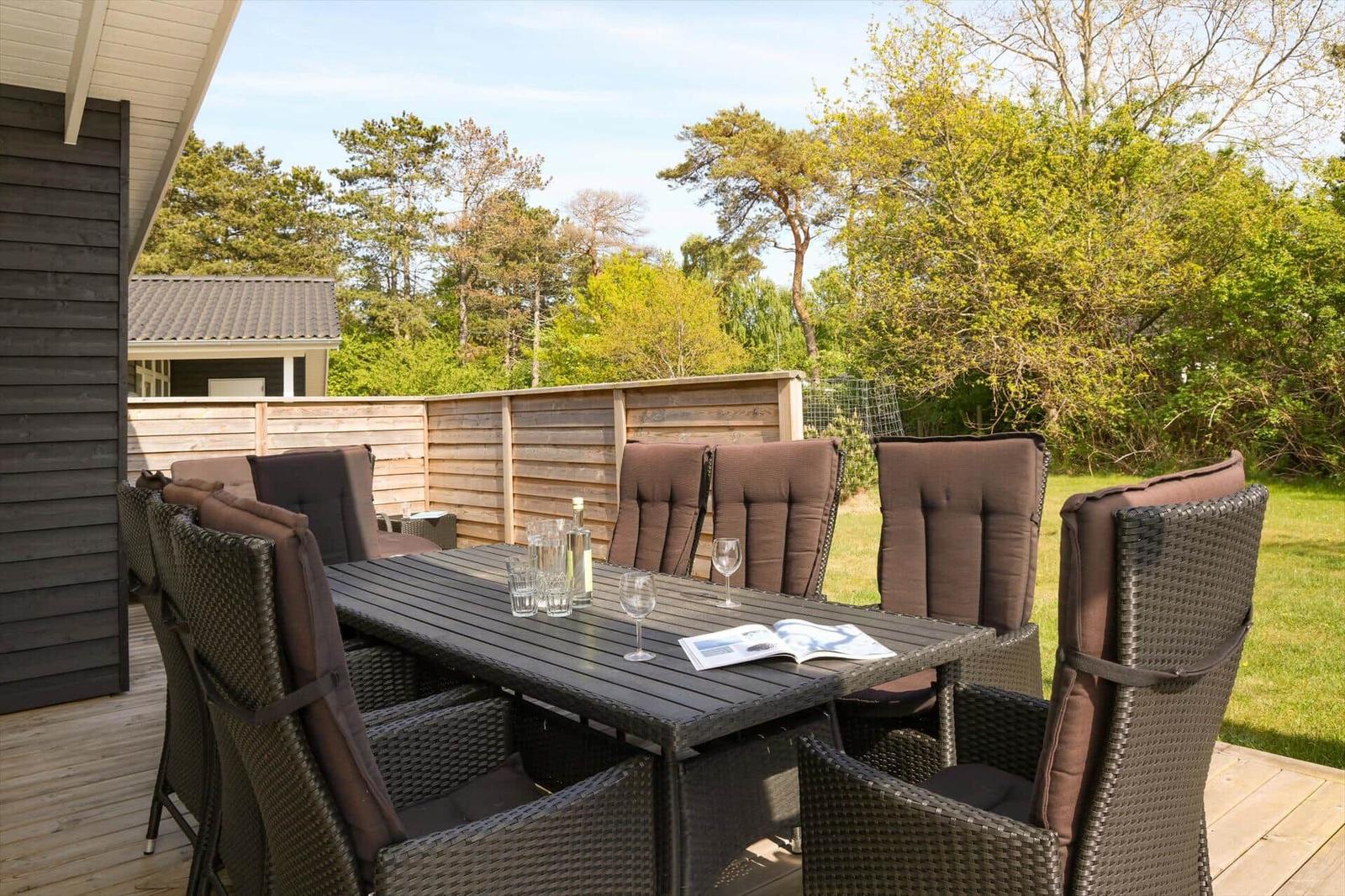 Terrasse mit Sitzgruppe und Tisch. Hintergrund: Holzzaun und Bäume.