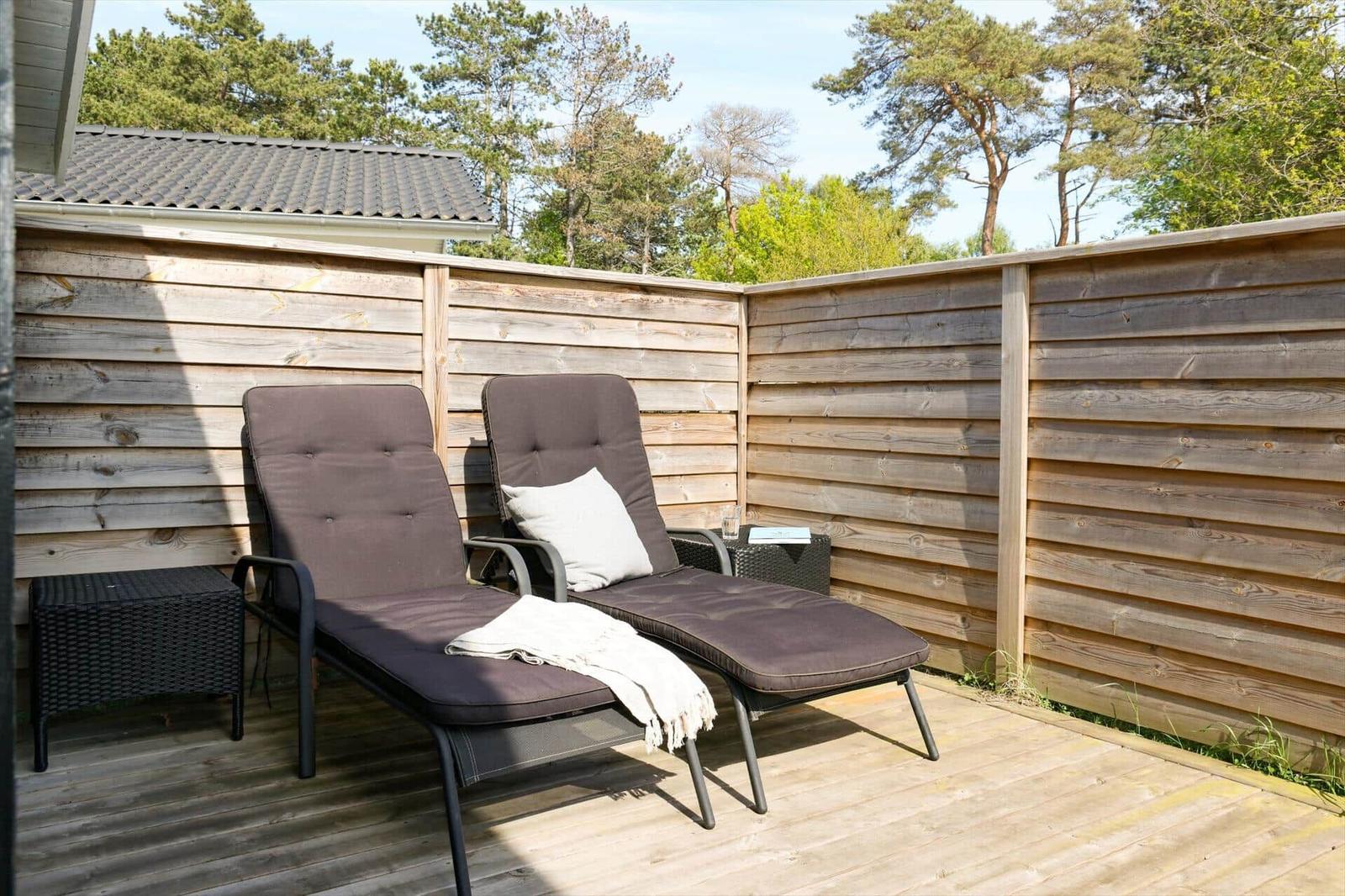 Terrasse mit zwei Liegestühlen, Holzwand und Blick auf Bäume.