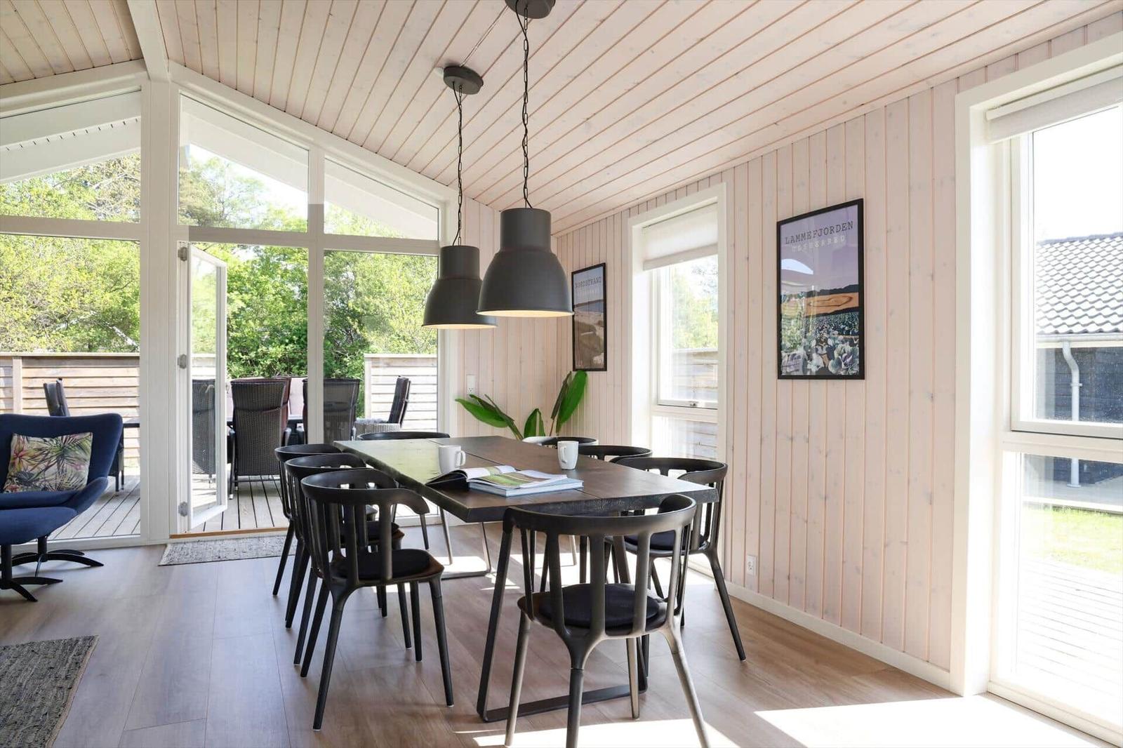 Essbereich mit Tisch, Stühlen und großen Fenstern. Draußen ist eine Terrasse mit Gartenmöbeln.