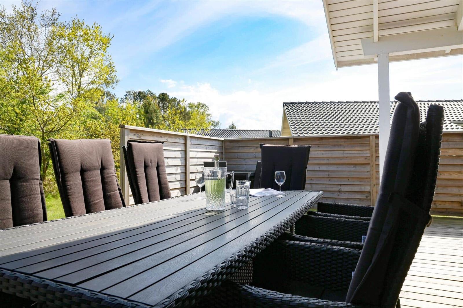 Terrasse mit Esstisch und Stühlen, umgeben von Holzzaun und Bäumen.