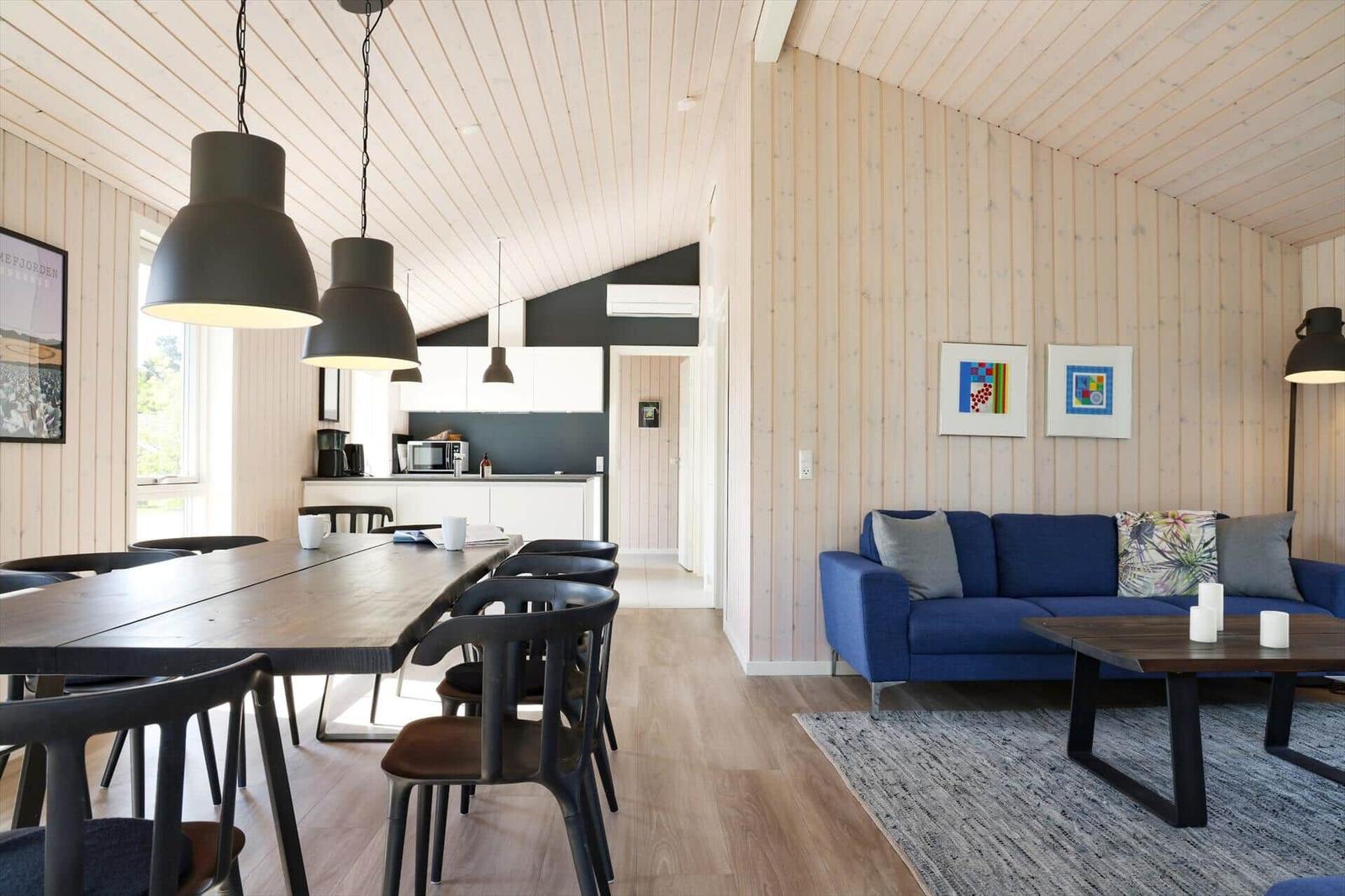 Wohn- und Essbereich mit Holzwand, blauem Sofa und Esstisch mit Stühlen.