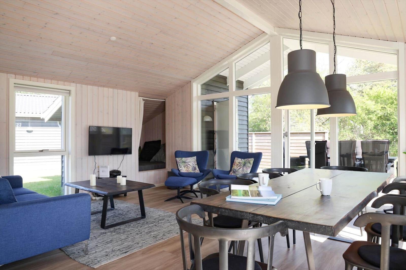 Wohn- und Essbereich mit Holzdecke, blauer Couch und großer Tisch