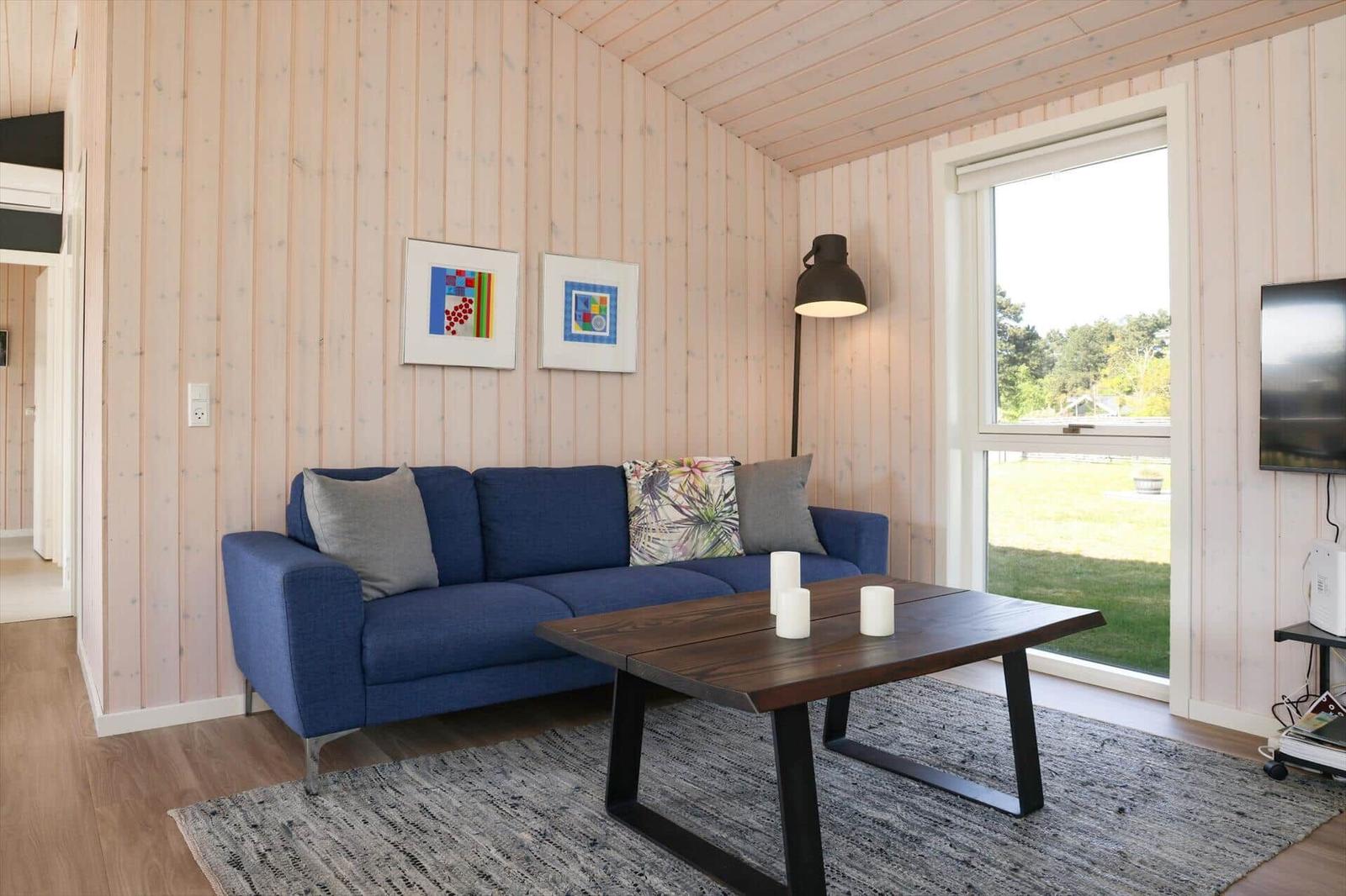 Ein Wohnzimmer mit blauem Sofa, Holztisch und Fensterblick auf Grünfläche.