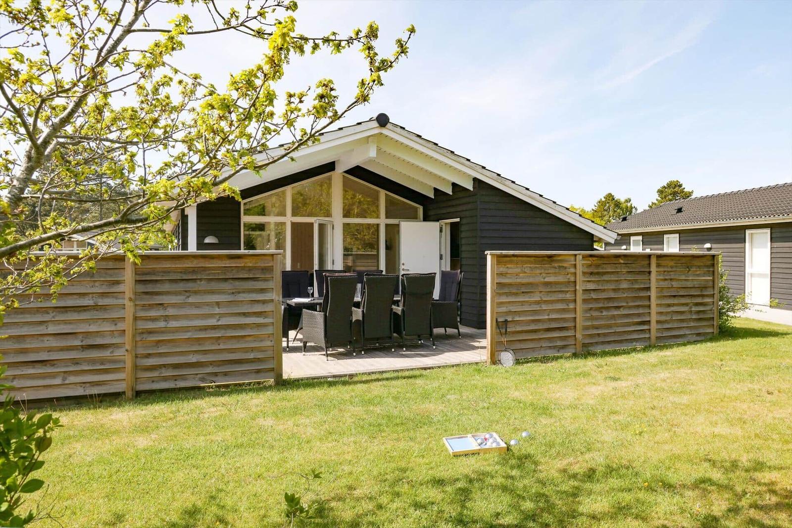 Haus mit Terrasse, Garten und Sitzgelegenheiten. Holzzaun umgibt den Außenbereich.