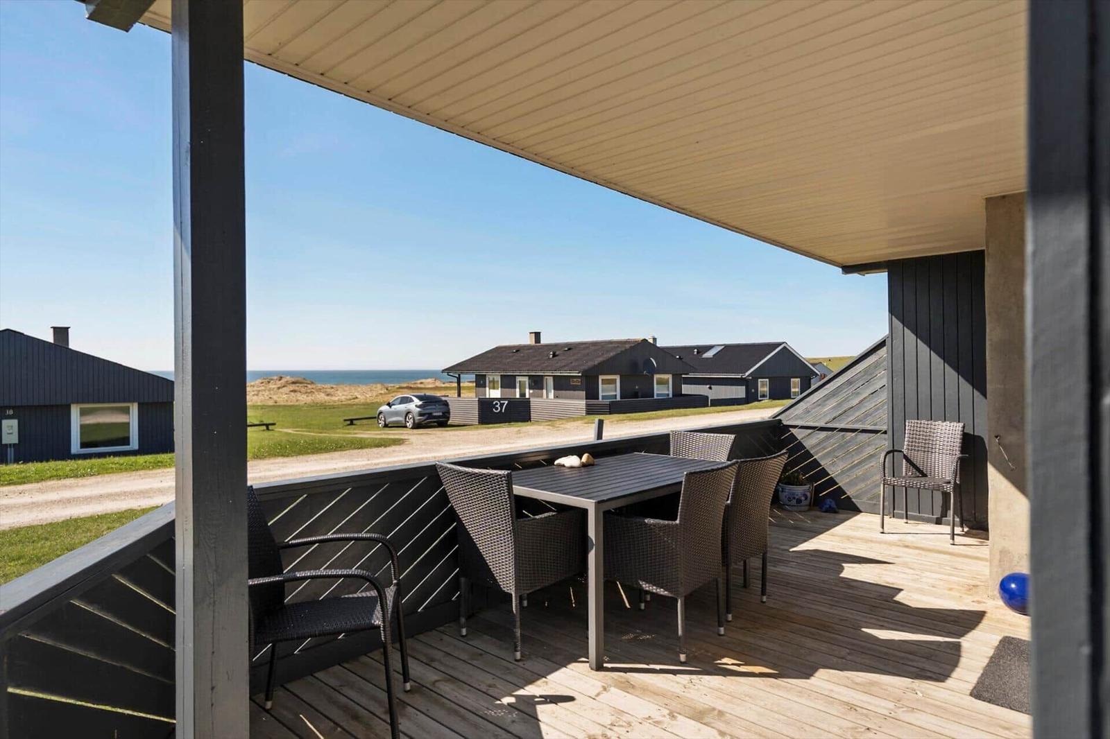 Terrasse mit Tisch und Stühlen. Blick auf Strand und Häuser.
