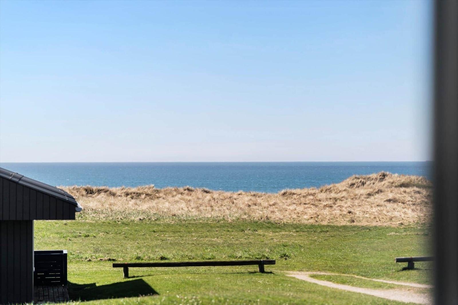 Ausblick auf das Meer mit Grasland und Holzbank im Vordergrund.