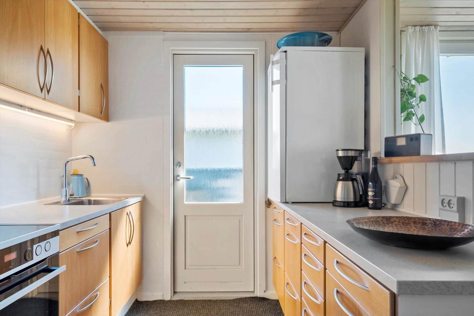 Küche mit Holzschränken, Kühlschrank und Glastür zur Außentür.
