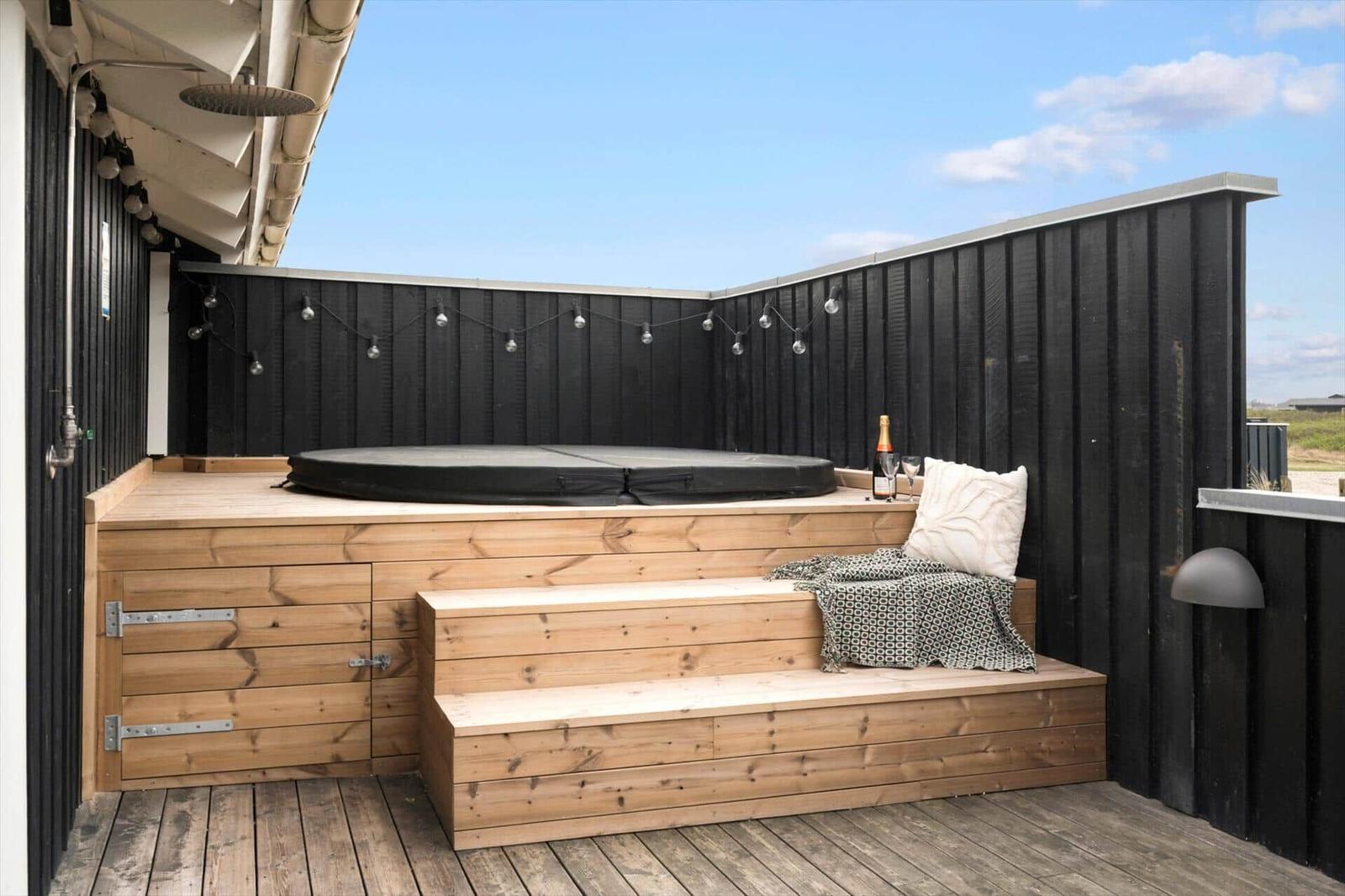 Terrasse mit Holzbank, Sprungmatte und Lichterkette an schwarzer Umzäunung.