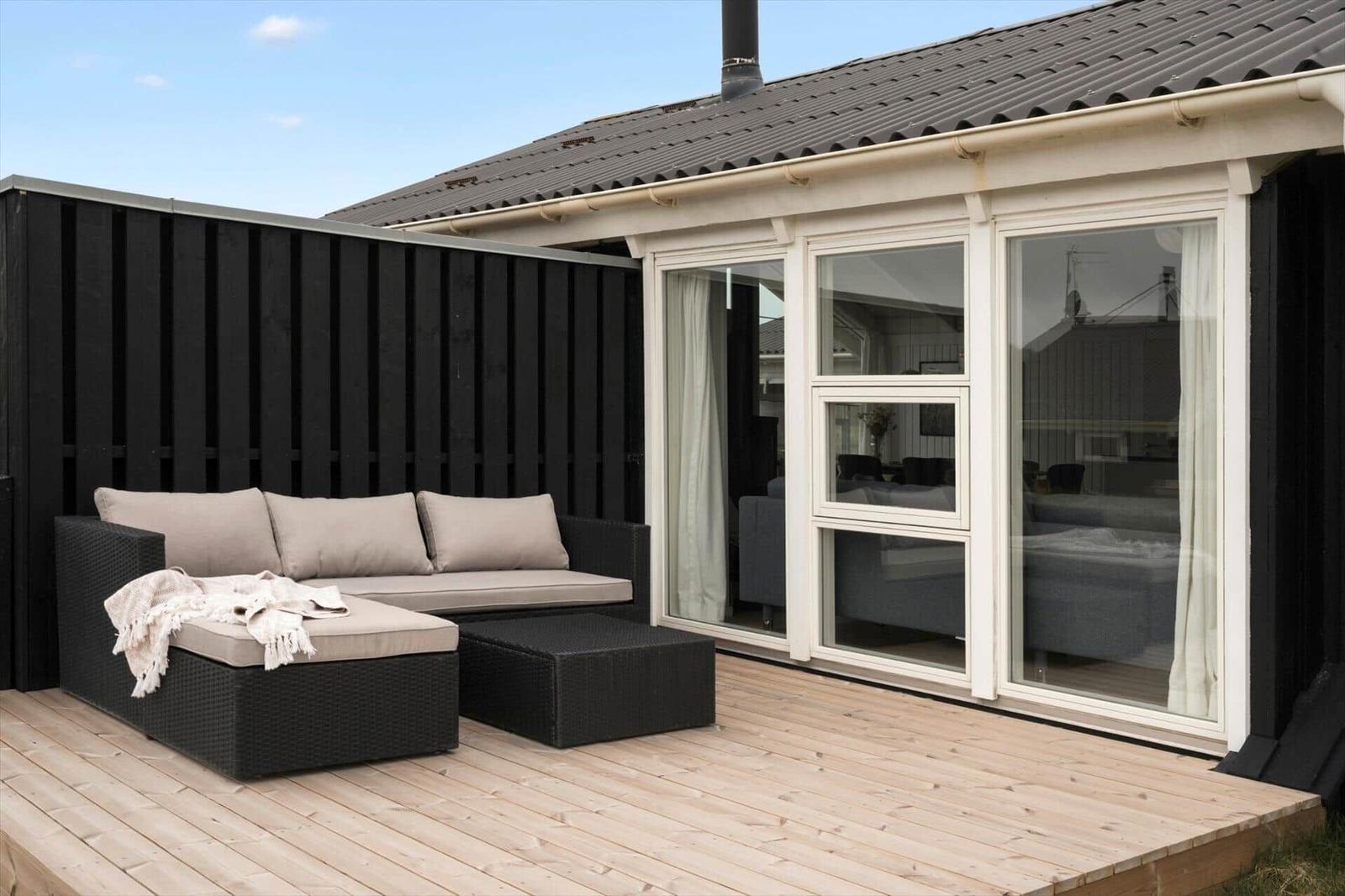 Terrasse mit Sitzgruppe und Blick ins Haus. Holzdeck und schwarze Wand.