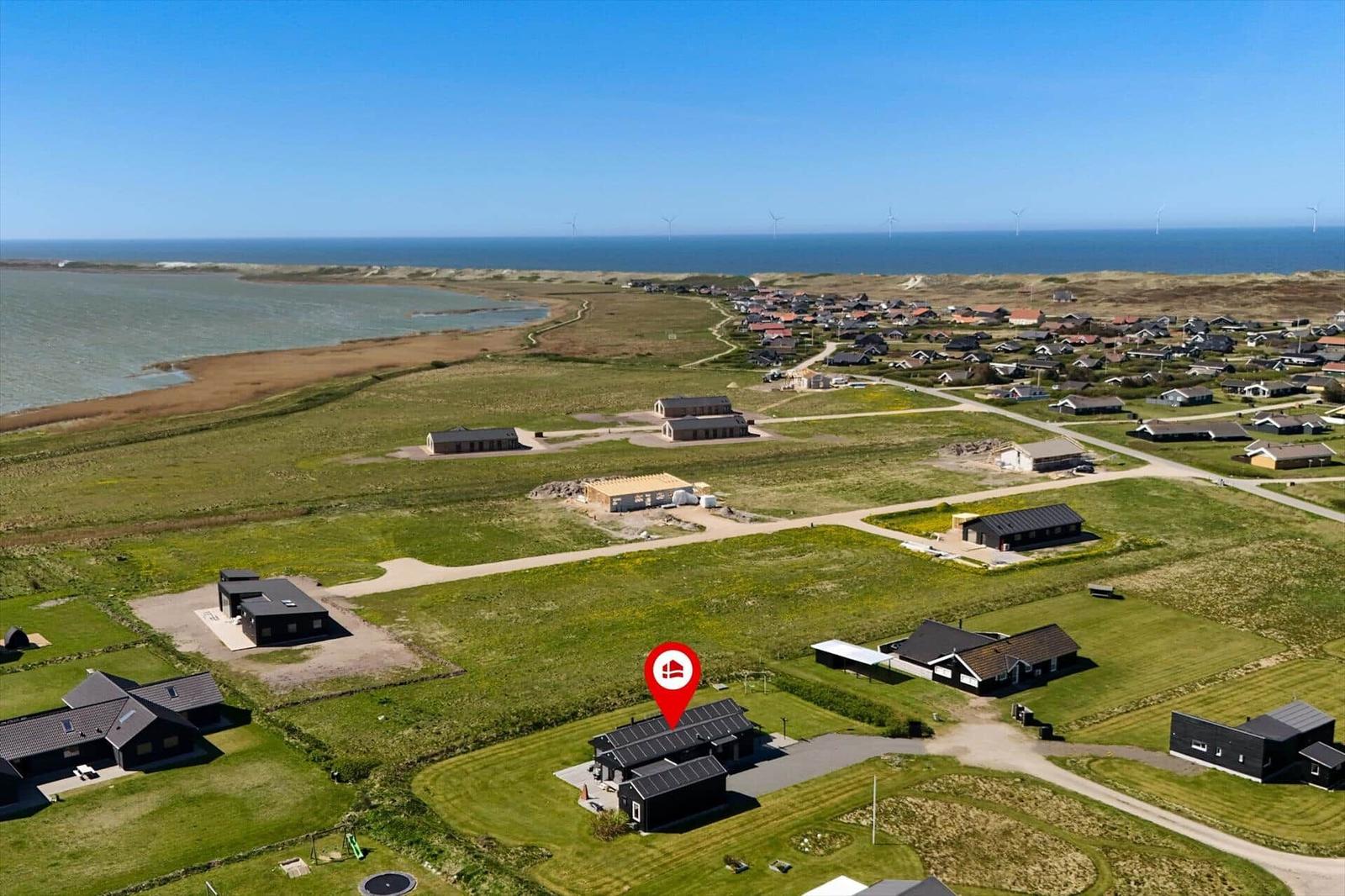 Haus mit Solaranlage in grüner Landschaft, nahe Strand und Windkraftanlagen.