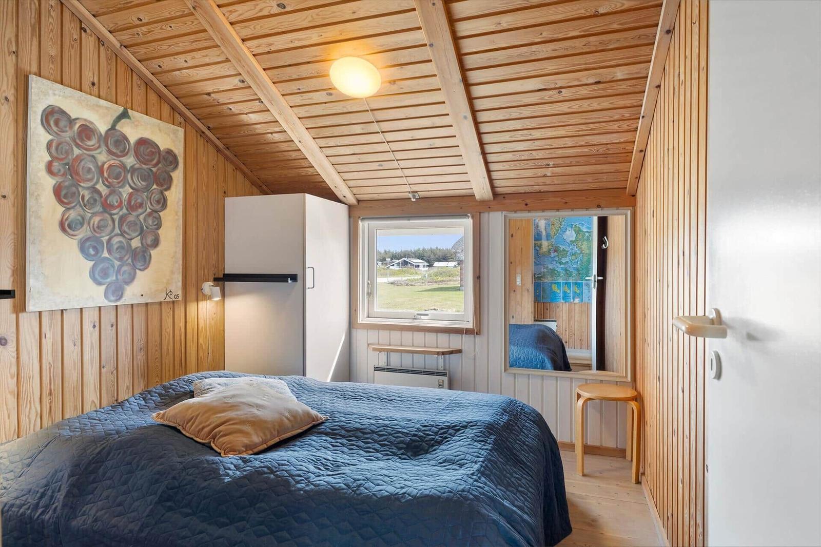 Schlafzimmer mit Holzwand, Bett, Fenster und Kühlschrank.